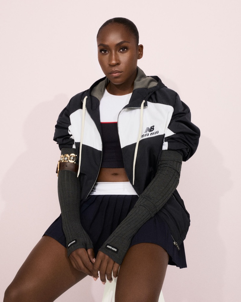 Coco Gauff wearing a black and white Miu Miu x New Balance jacket with long ribbed arm warmers and a pleated tennis skirt