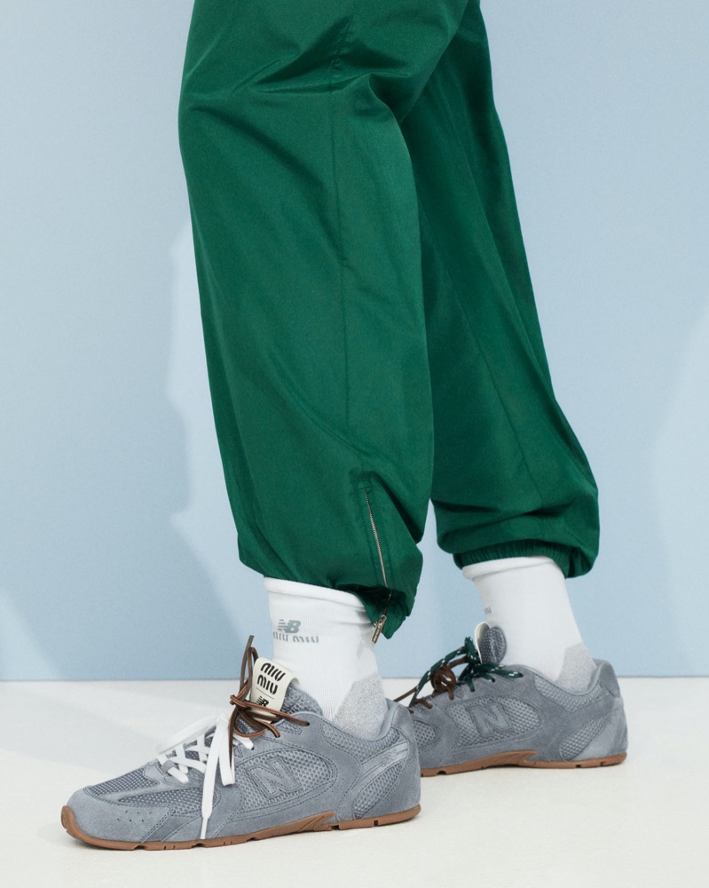 Close-up of silver and grey Miu Miu x New Balance sneakers with gum soles worn with white branded socks and green pants