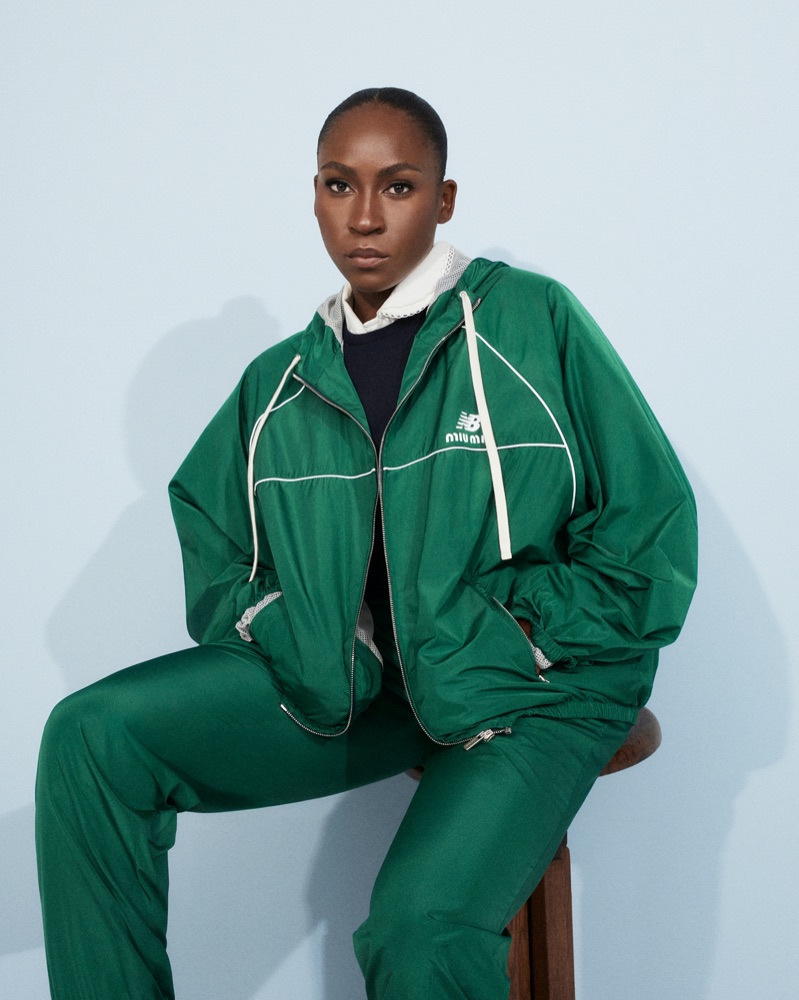 Coco Gauff in a green Miu Miu x New Balance tracksuit with white trim and zipped jacket sitting against a light blue background