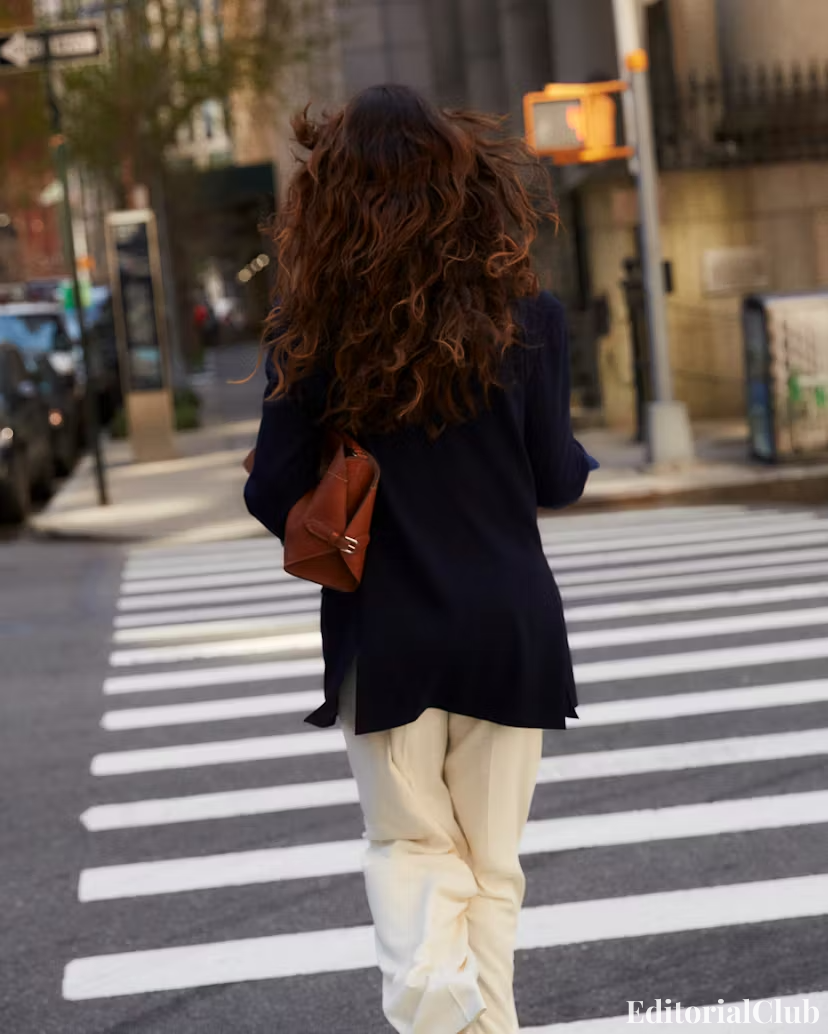 Eiza González walking across New York crosswalk from behind in navy blazer and cream trousers – city fashion moment.