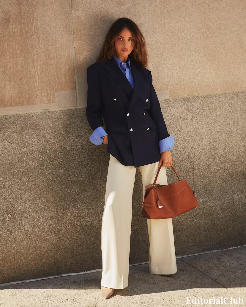 Eiza González standing against stone wall in cream pants and double-breasted Ralph Lauren blazer – powerful urban style.