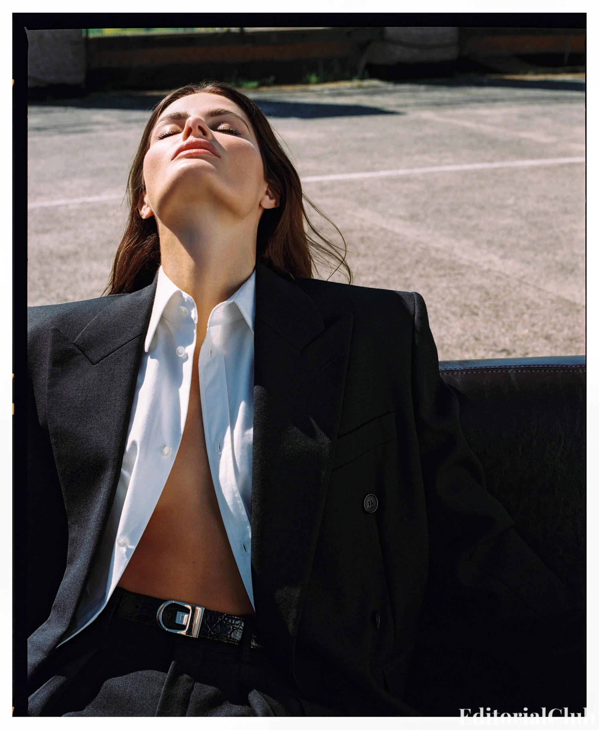 Editorial-style image of Isabeli Fontana reclining on a rooftop in an open black suit jacket and crisp white shirt.