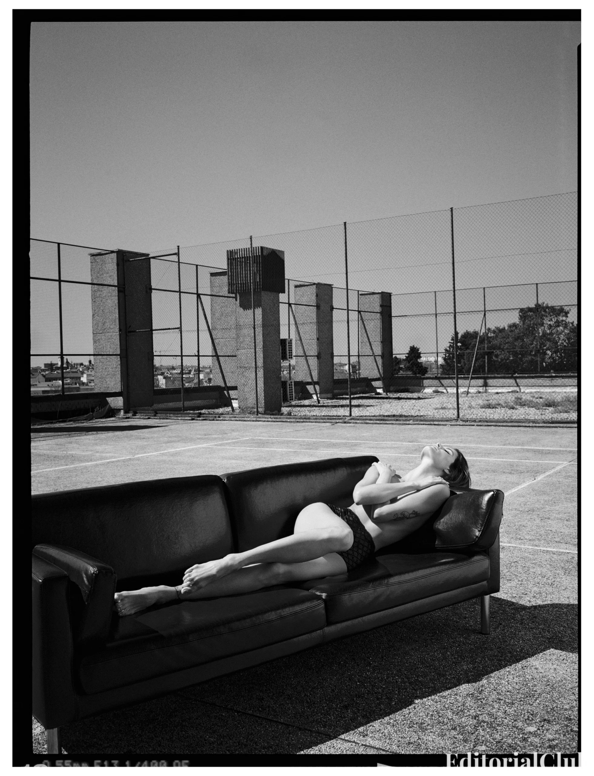 Isabeli Fontana sunbathing topless on a leather couch on a rooftop tennis court in black and white for Numéro Netherlands May 2025.