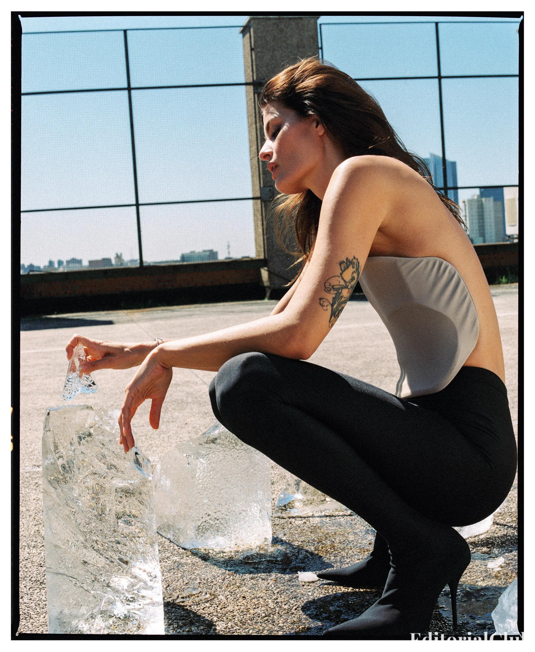 Isabeli Fontana in a backless bodysuit and black tights crouching beside melting ice blocks on a rooftop shoot for Numéro Netherlands May 2025.