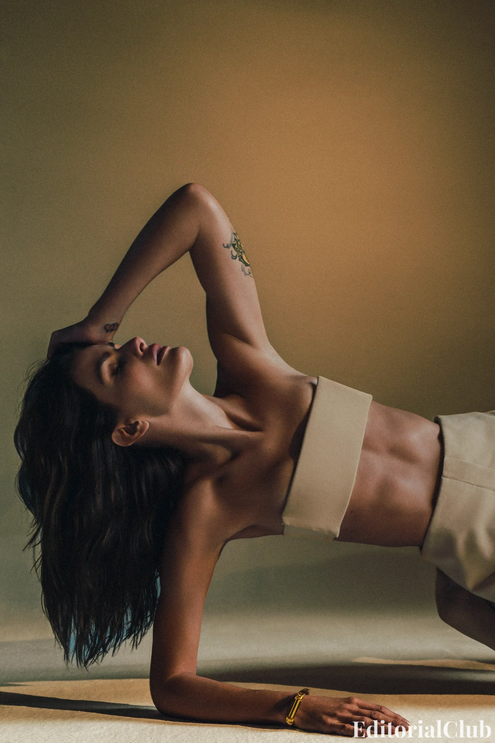 Isabeli Fontana reclining on the floor in a beige bandeau set, showing her tattoos and sharp lighting contrasts in Numéro Netherlands May 2025.