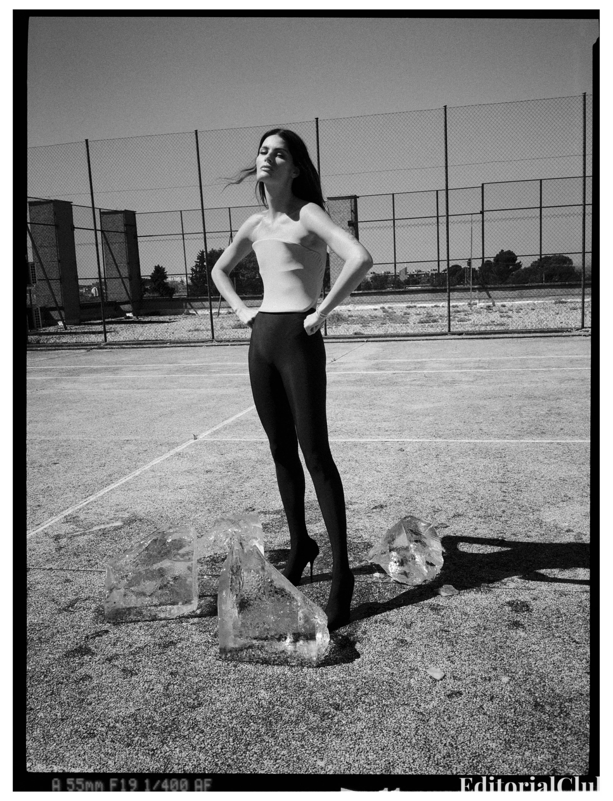 Isabeli Fontana standing confidently in black leggings and a white top on an outdoor court, surrounded by large ice blocks.
