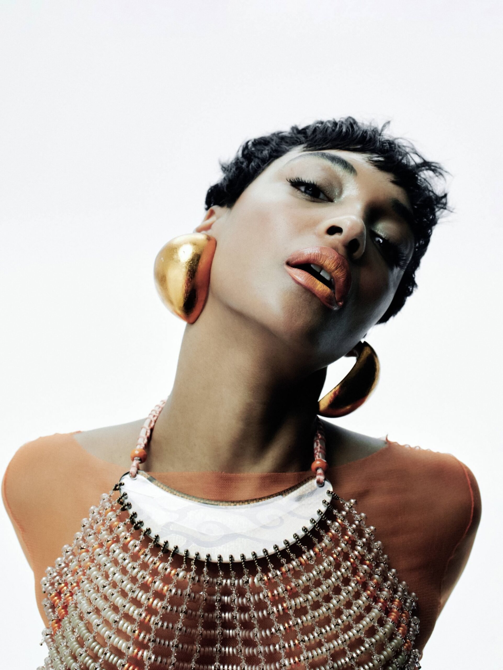 Close-up of Jourdan Dunn wearing bold gold earrings and beaded necklace for Harper’s Bazaar editorial