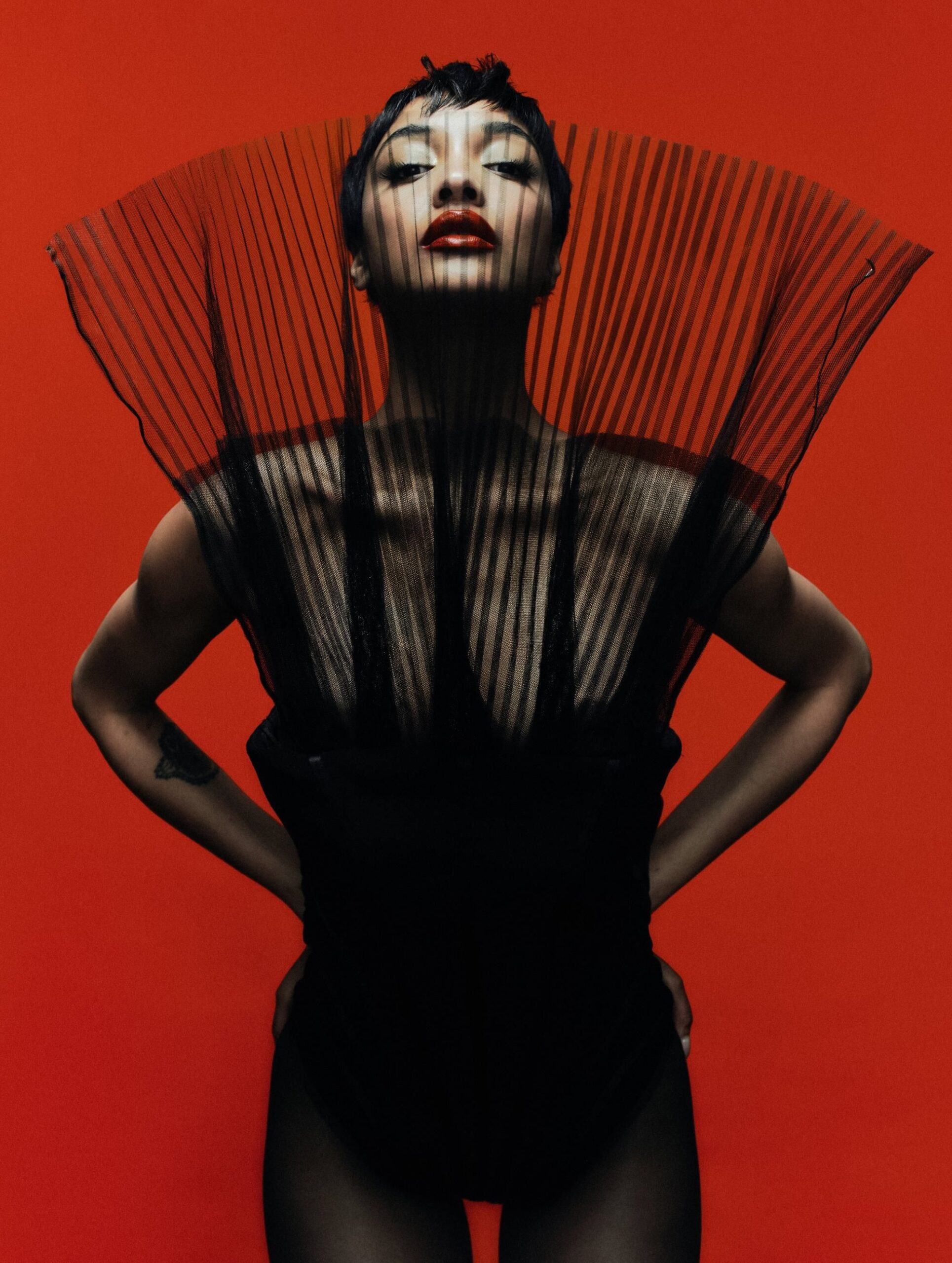 Jourdan Dunn in a sheer structured black bodysuit with pleated neckline on a red backdrop
