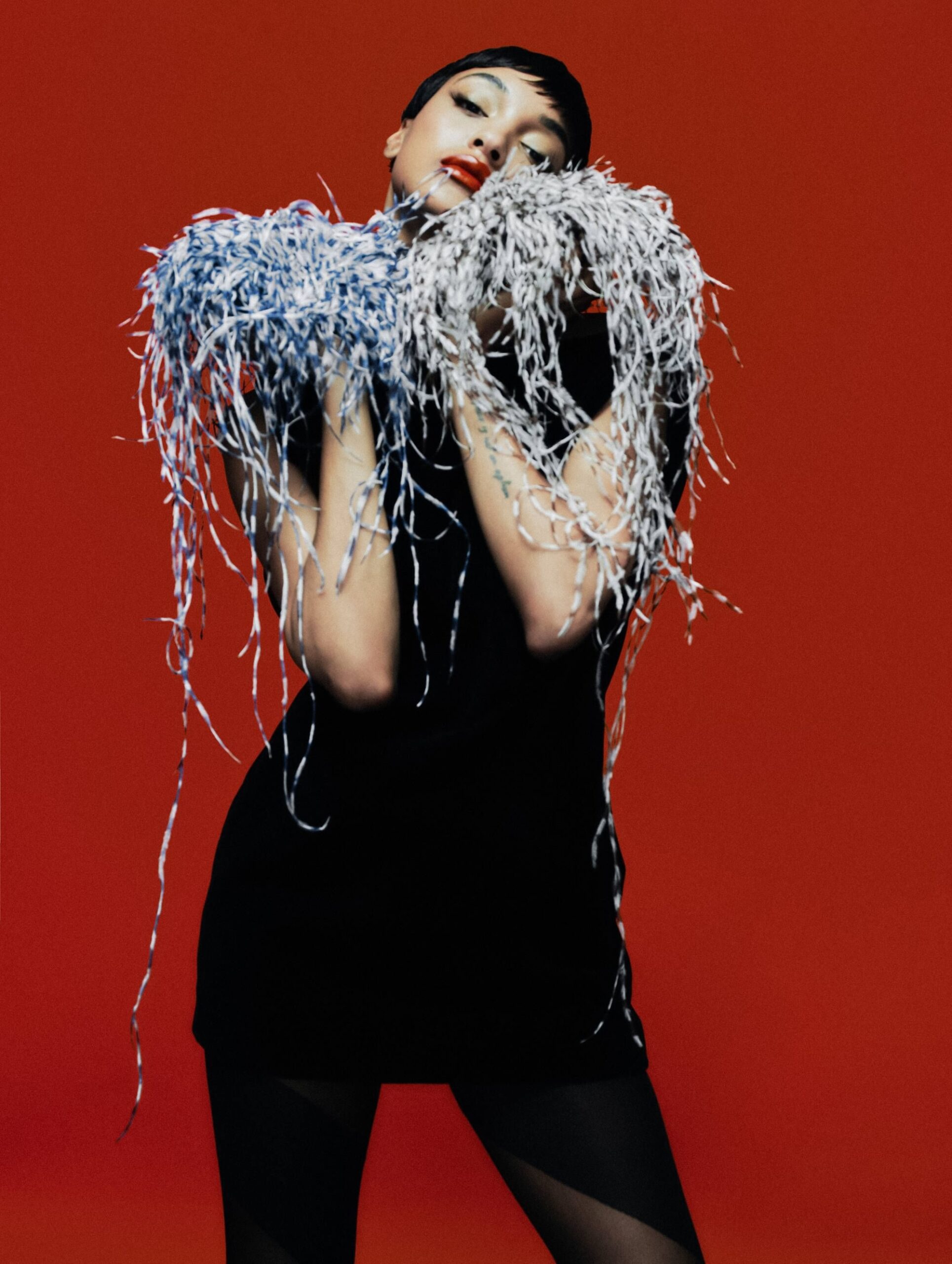Jourdan Dunn holding shredded fabric details in a playful pose against a red background