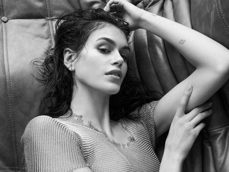 Kaia Gerber lying on a leather couch in a mesh dress, captured in a soft monochrome portrait