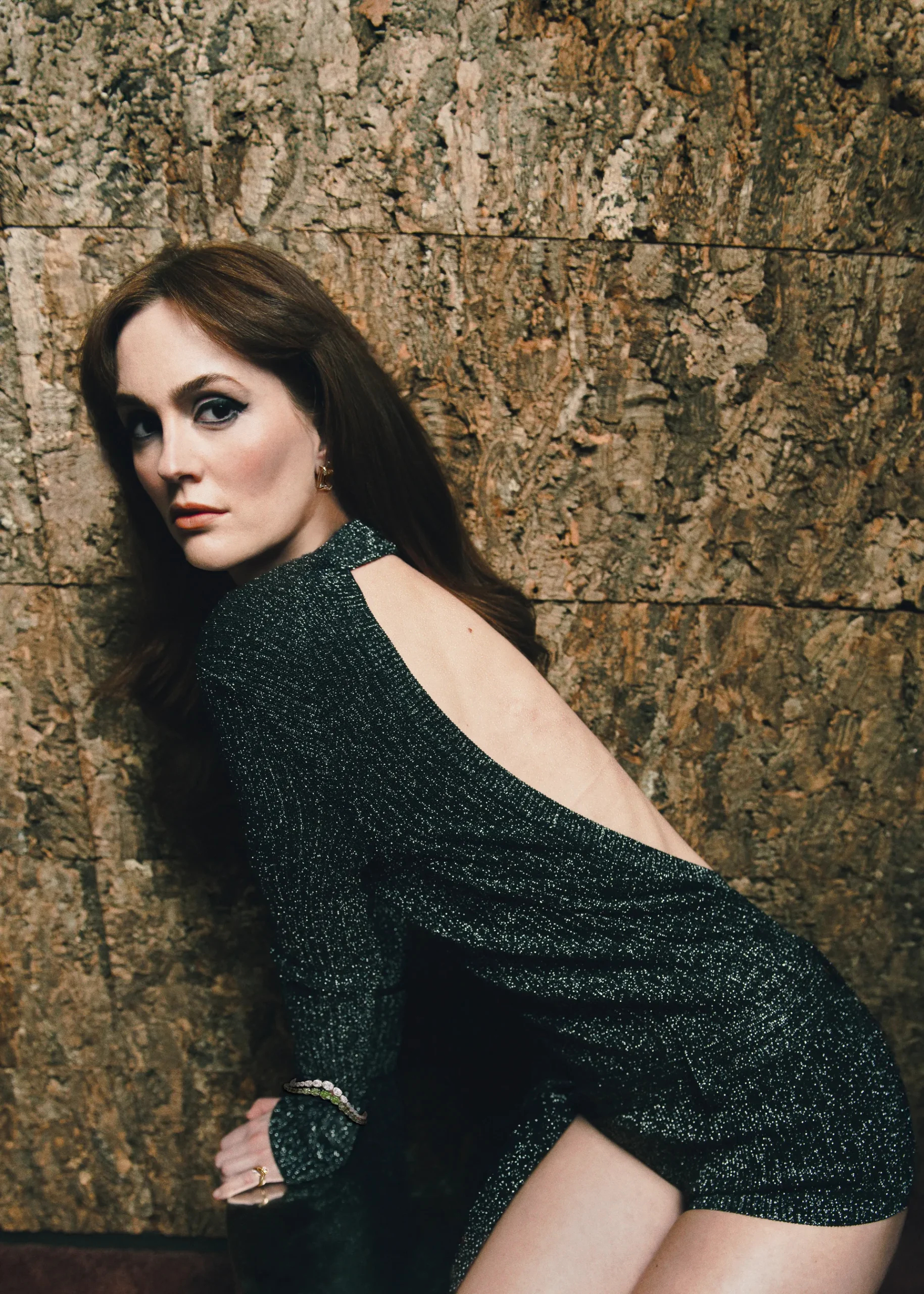 Leighton Meester in a sparkly open-back mini dress, leaning against a textured wall in a dramatic editorial portrait.