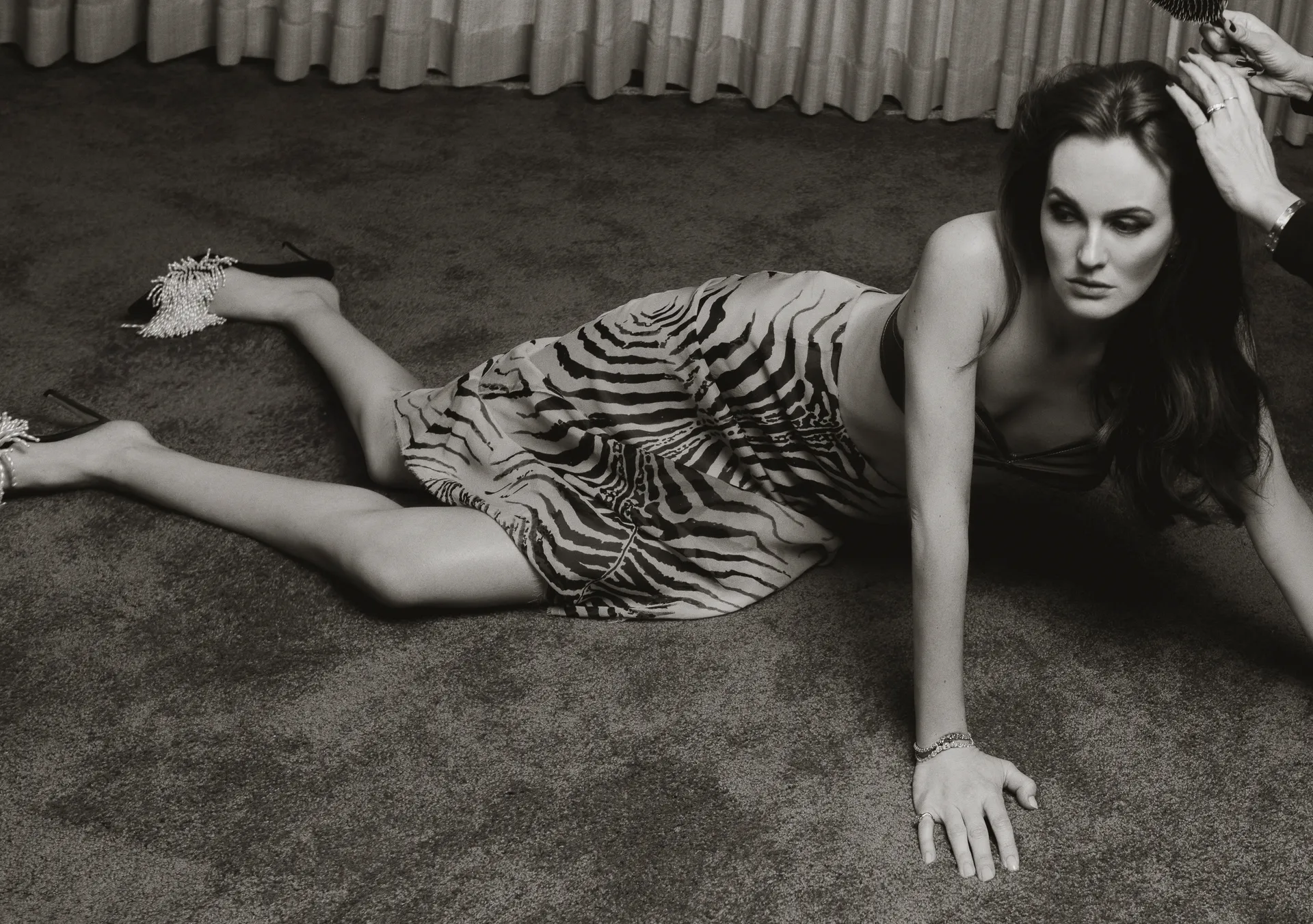 Leighton Meester in a zebra-print skirt and bandeau top, as a stylist adjusts her hair during a behind-the-scenes moment in a black-and-white shot.