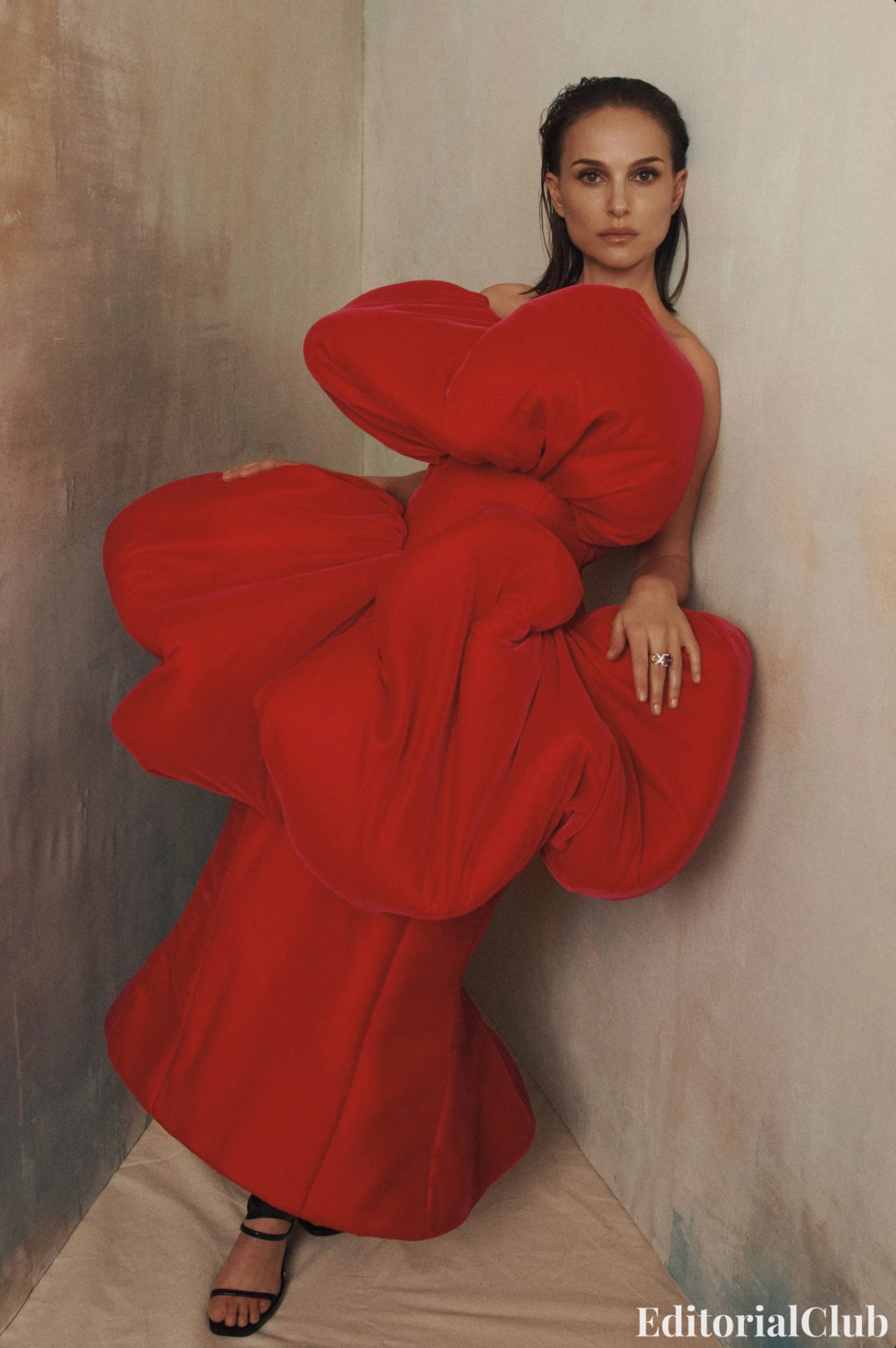 Natalie Portman leans in a corner wearing a sculptural red gown with oversized bows for Vogue Australia May 2025, photographed by Lachlan Bailey