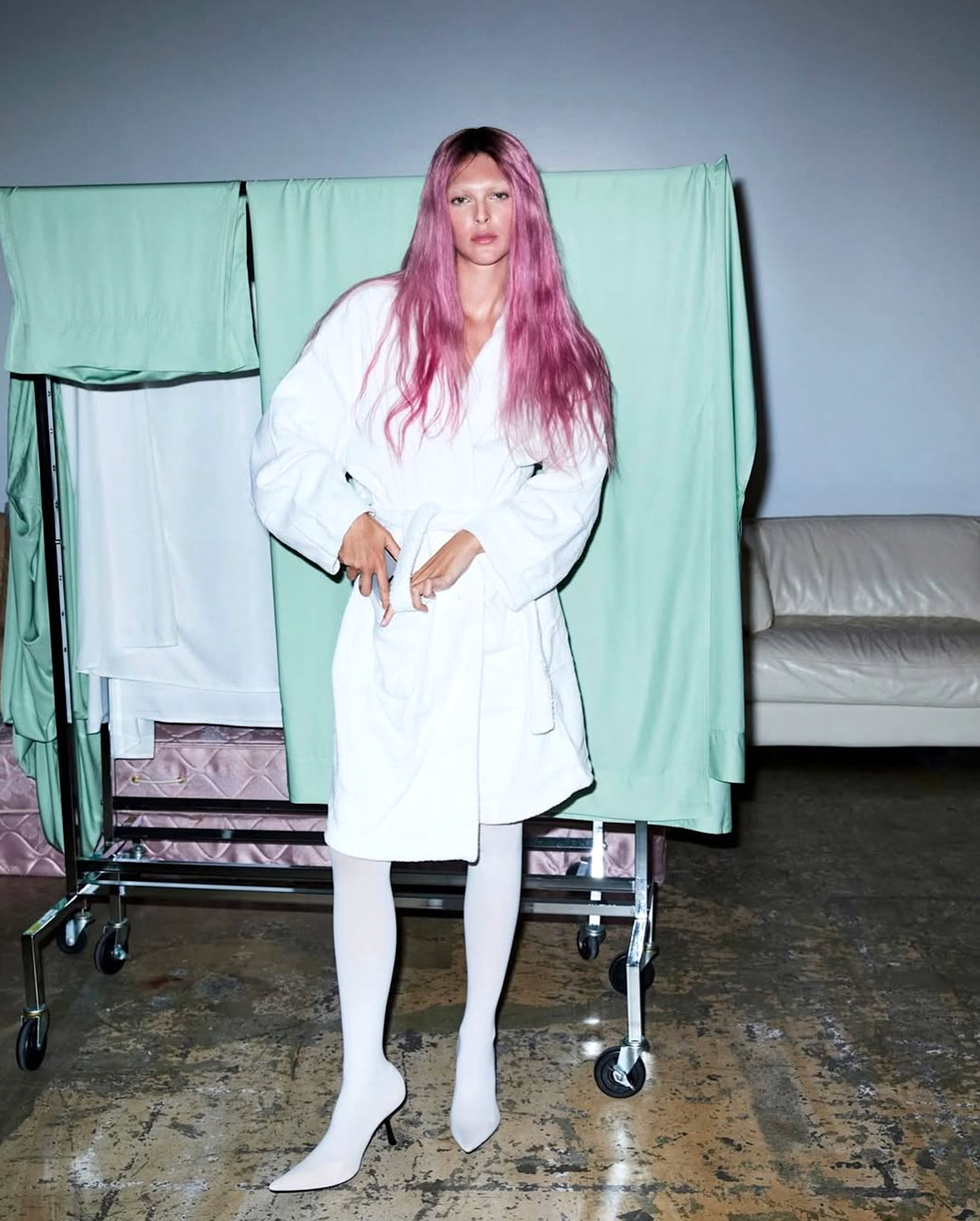 Vittoria Ceretti in a white robe and tights with pink hair, standing in front of pastel green fabrics and studio lighting, Vogue France April 2025.