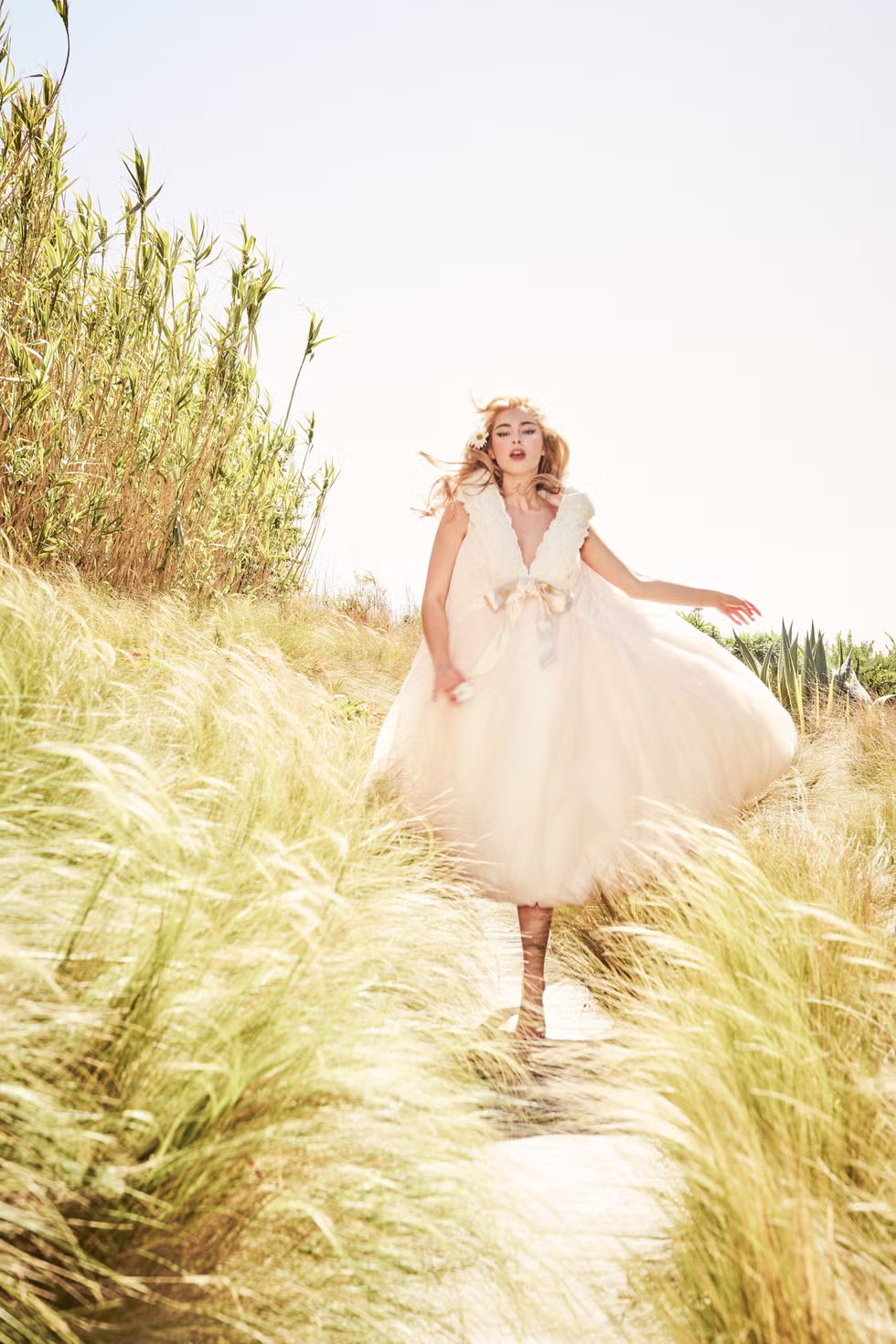Addison Rae running down a sunlit path in a voluminous ivory dress adorned with floral accents