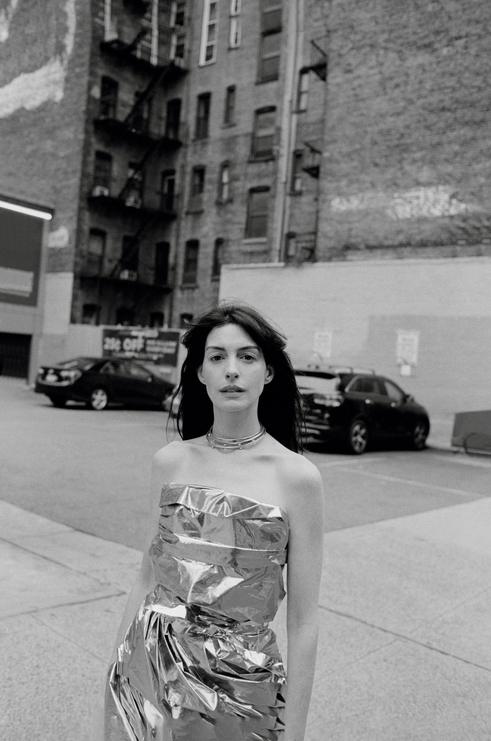 Anne Hathaway walking through a city street in a reflective metallic foil dress, captured in black and white for Vogue France's November 2024 editorial.