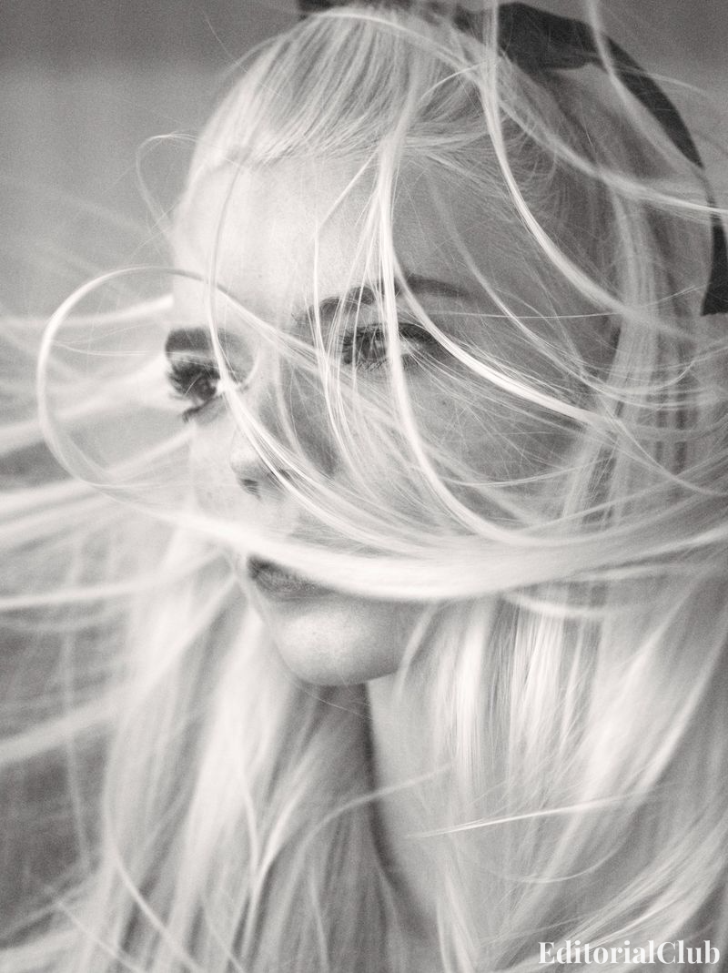 Windblown close-up of Anya Taylor-Joy with strands of her platinum hair sweeping across her face, captured in black and white.