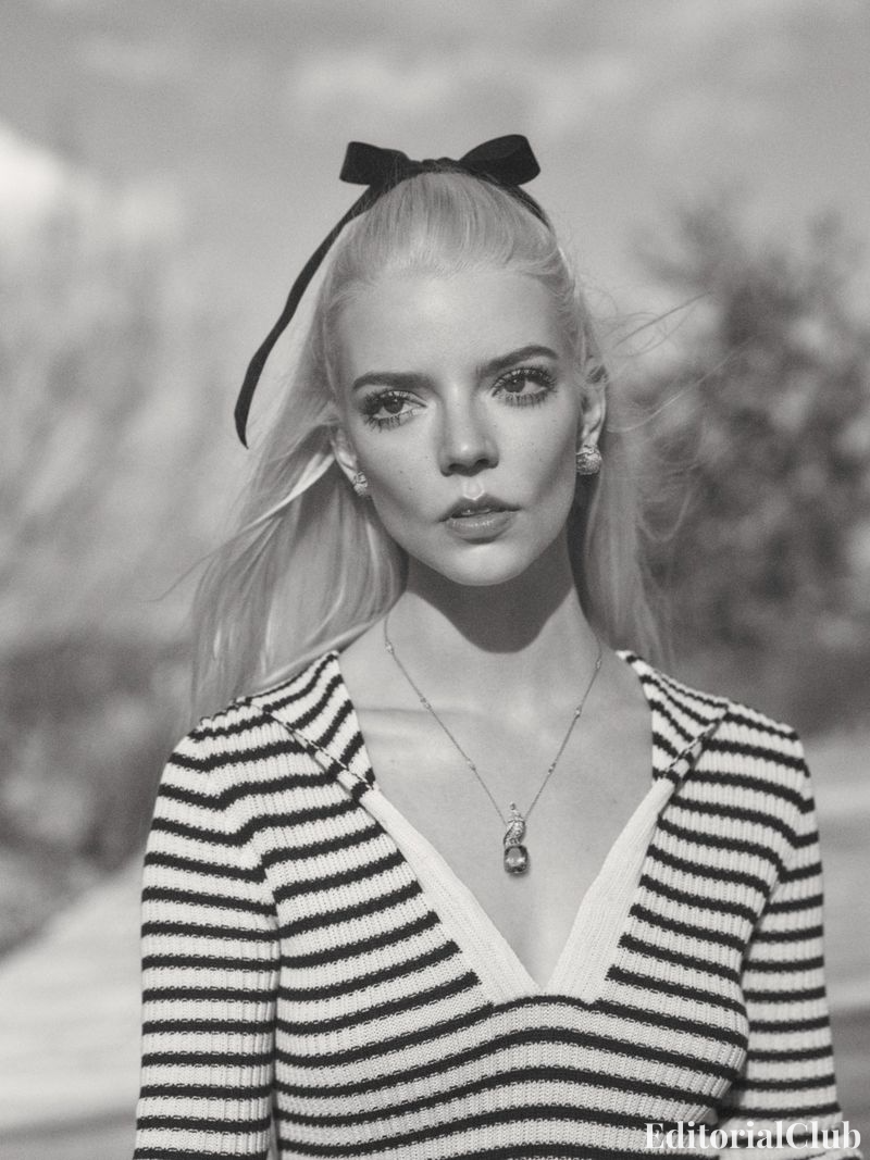 Monochrome portrait of Anya Taylor-Joy in a striped knit top with a plunging neckline, accessorized with a pendant and hair ribbon.