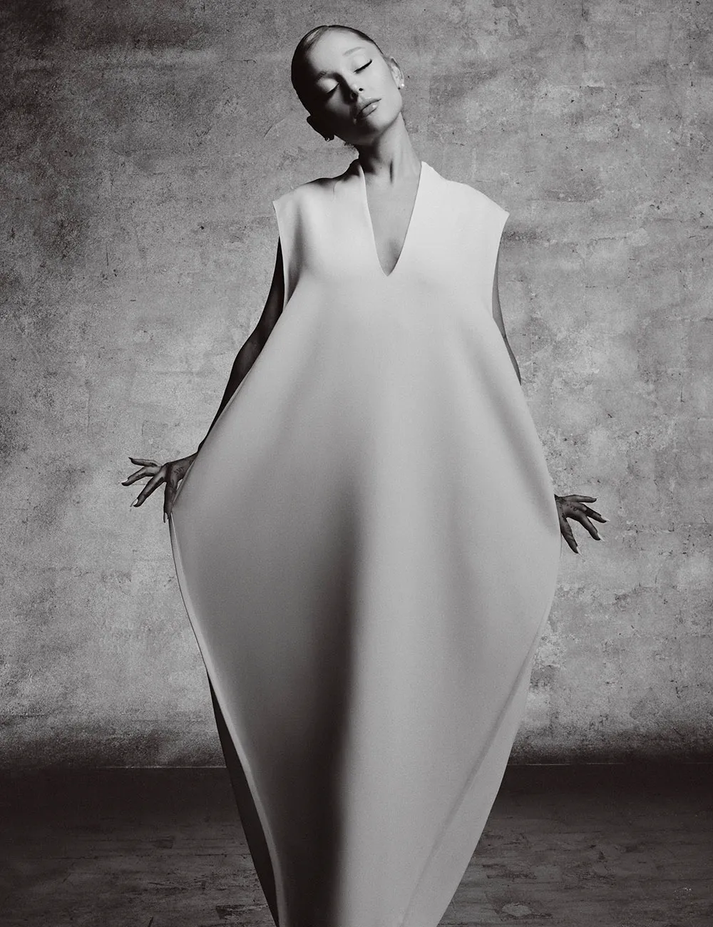 Ariana Grande in an egg-shaped, sculptural white gown, eyes closed in a serene pose, black and white editorial.