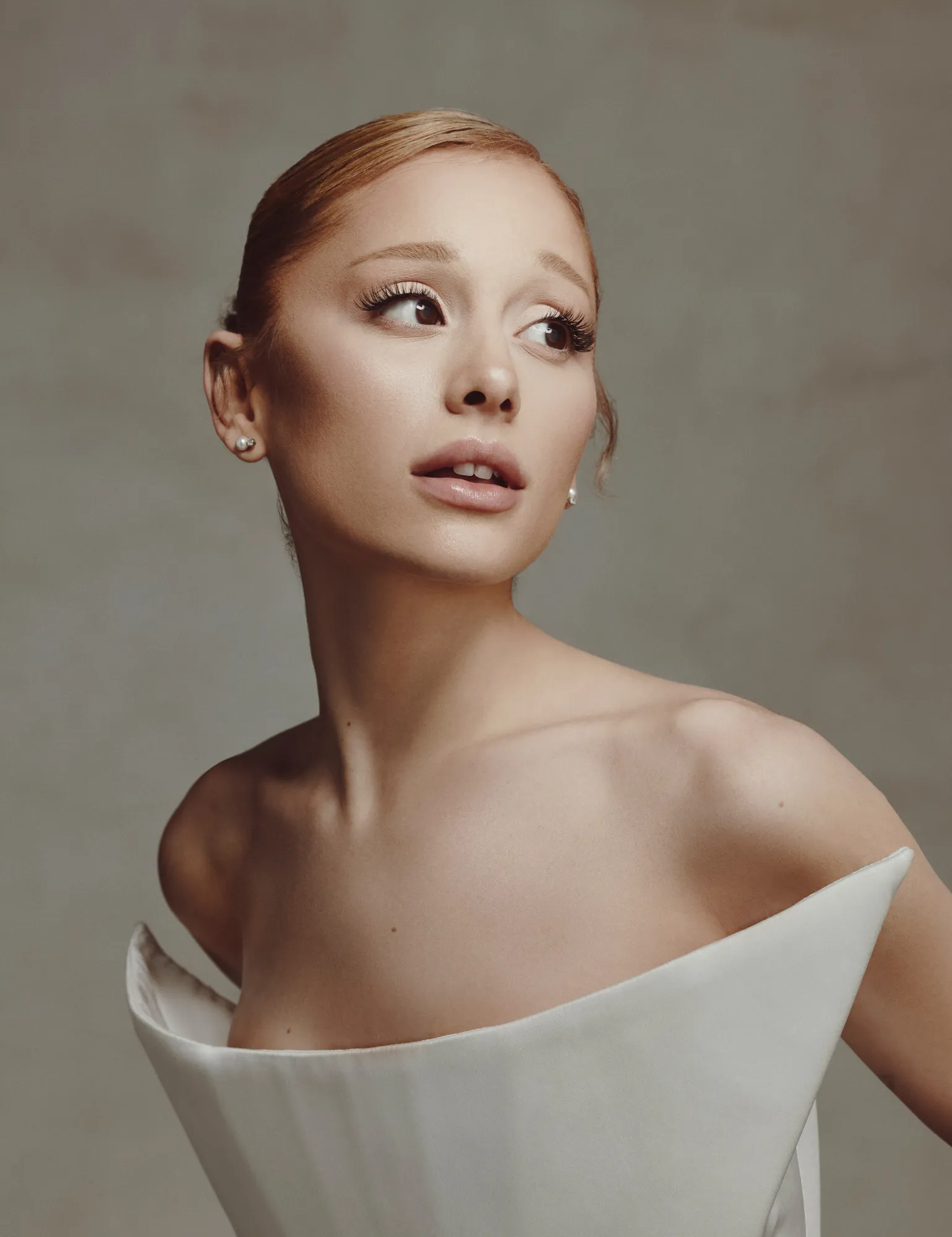 Ariana Grande in a minimalist off-shoulder sculptural white gown, glancing sideways in a portrait from The Hollywood Reporter February 2025 photoshoot.