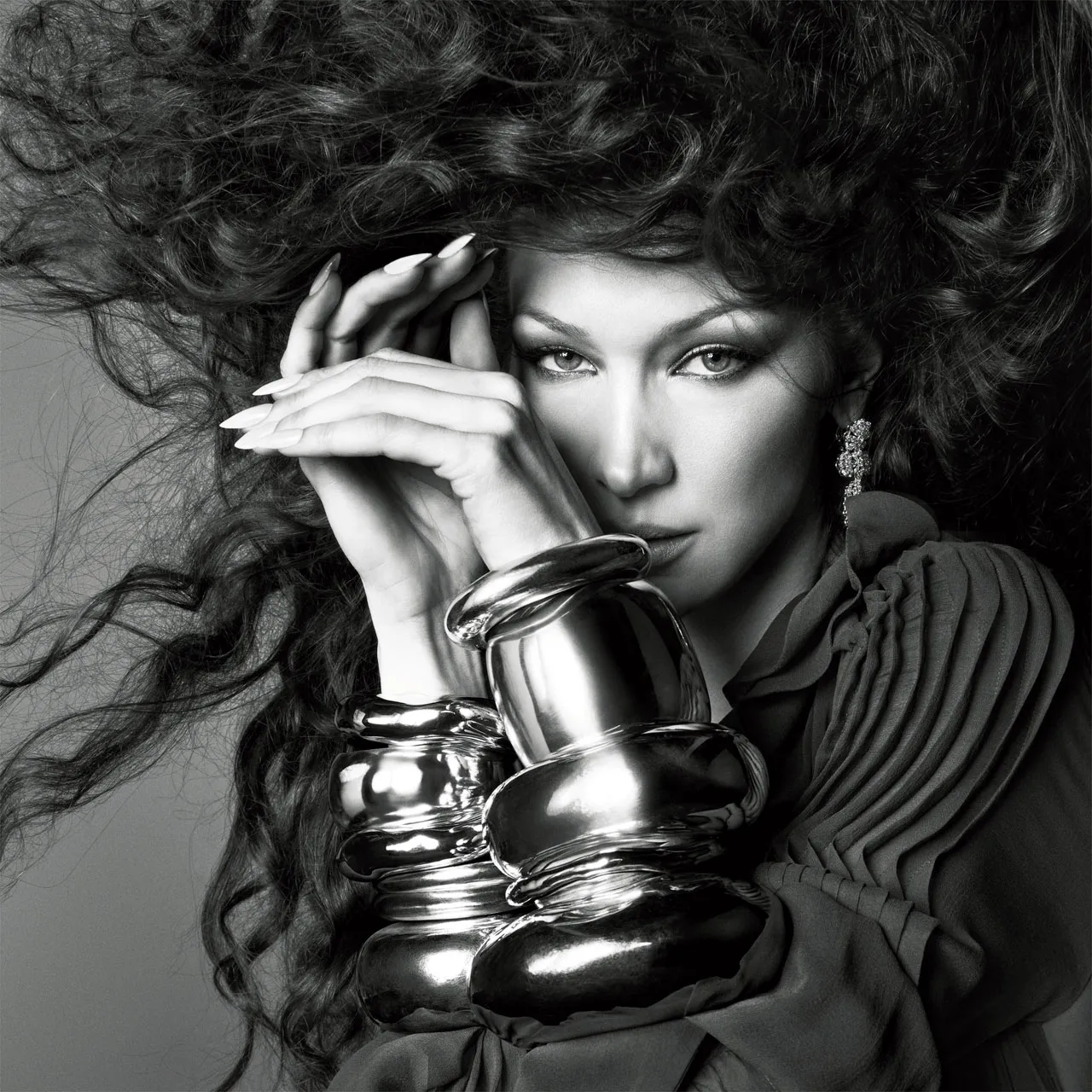 Bella Hadid close-up in dramatic lighting, wearing oversized silver bangles and voluminous curls for British Vogue June 2025.