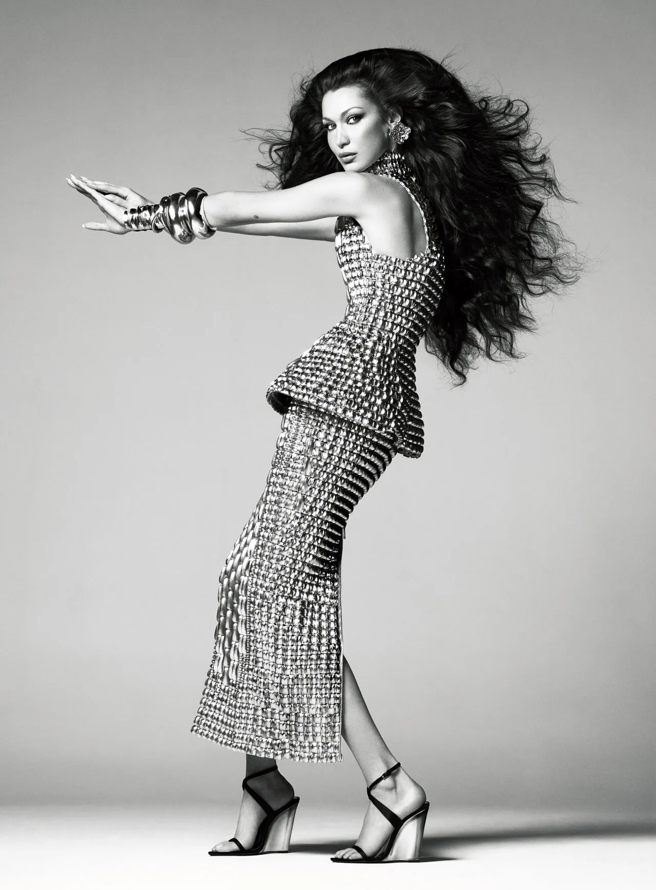 Bella Hadid strikes a dynamic pose in a metallic woven two-piece outfit with platform heels, featured in British Vogue June 2025.