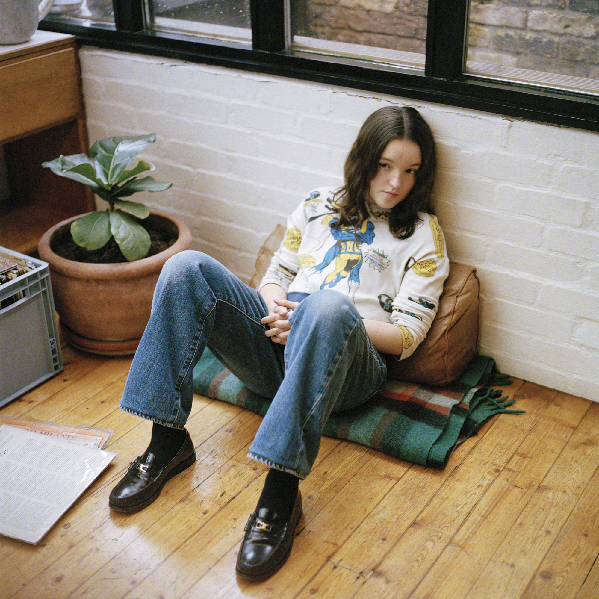 Bella Ramsey sits on the floor in casual jeans and a graphic sweatshirt during Interview Magazine shoot, May 2025