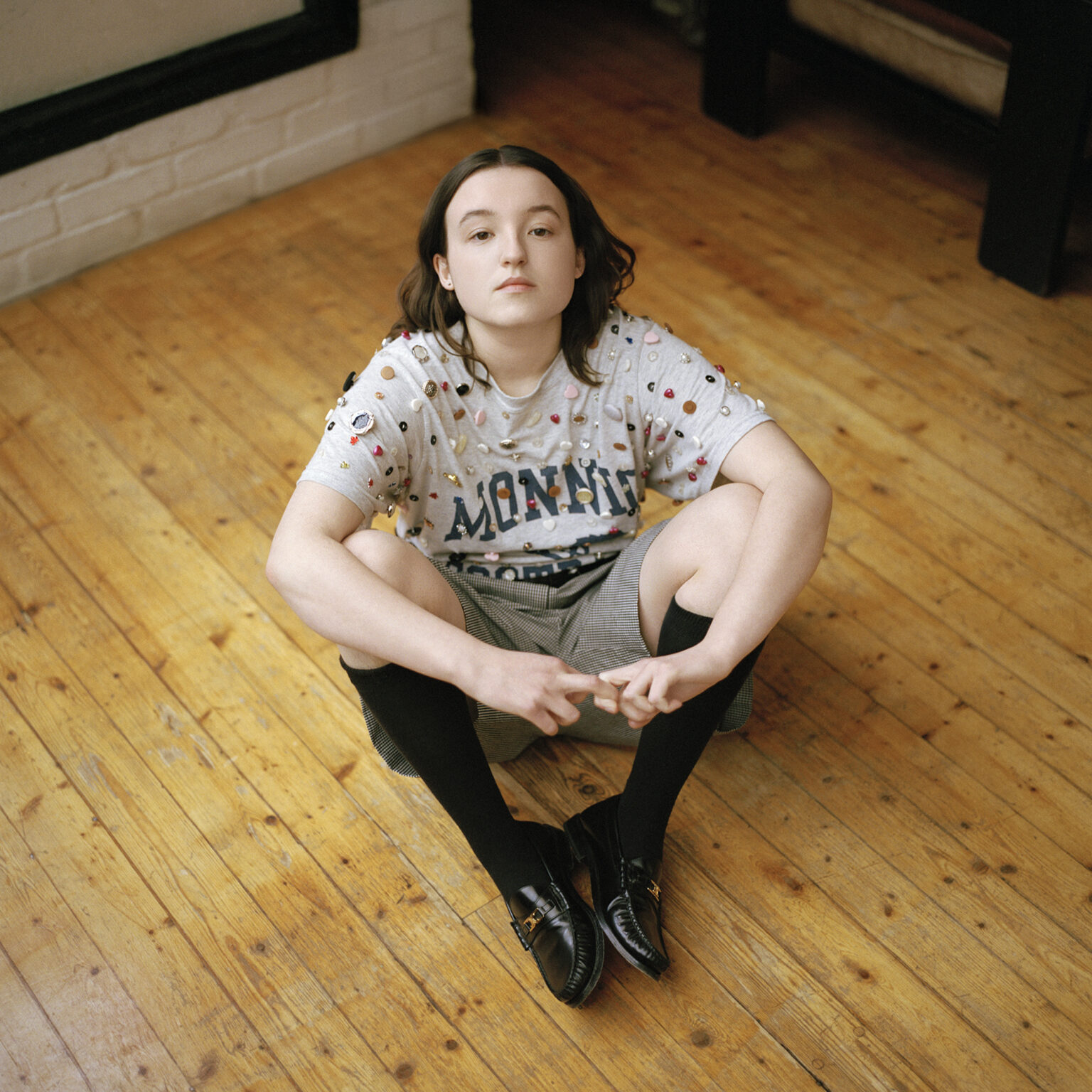 Bella Ramsey poses on wooden flooring in knee-high socks and embellished tee for Interview Magazine photo series, May 2025