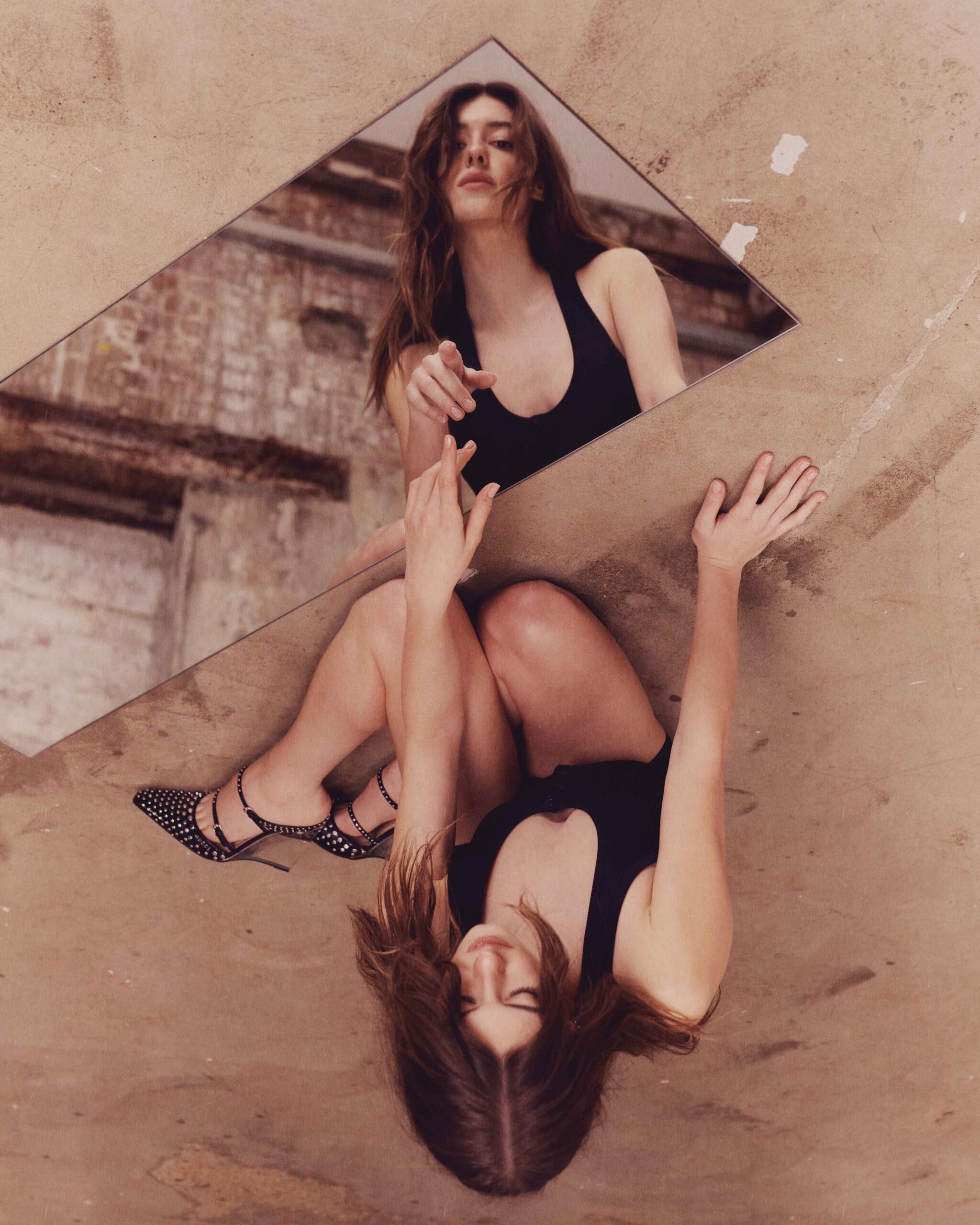 Daisy Edgar-Jones crouches on the ground in a black outfit, gazing into a mirror placed diagonally, reflecting her striking pose.