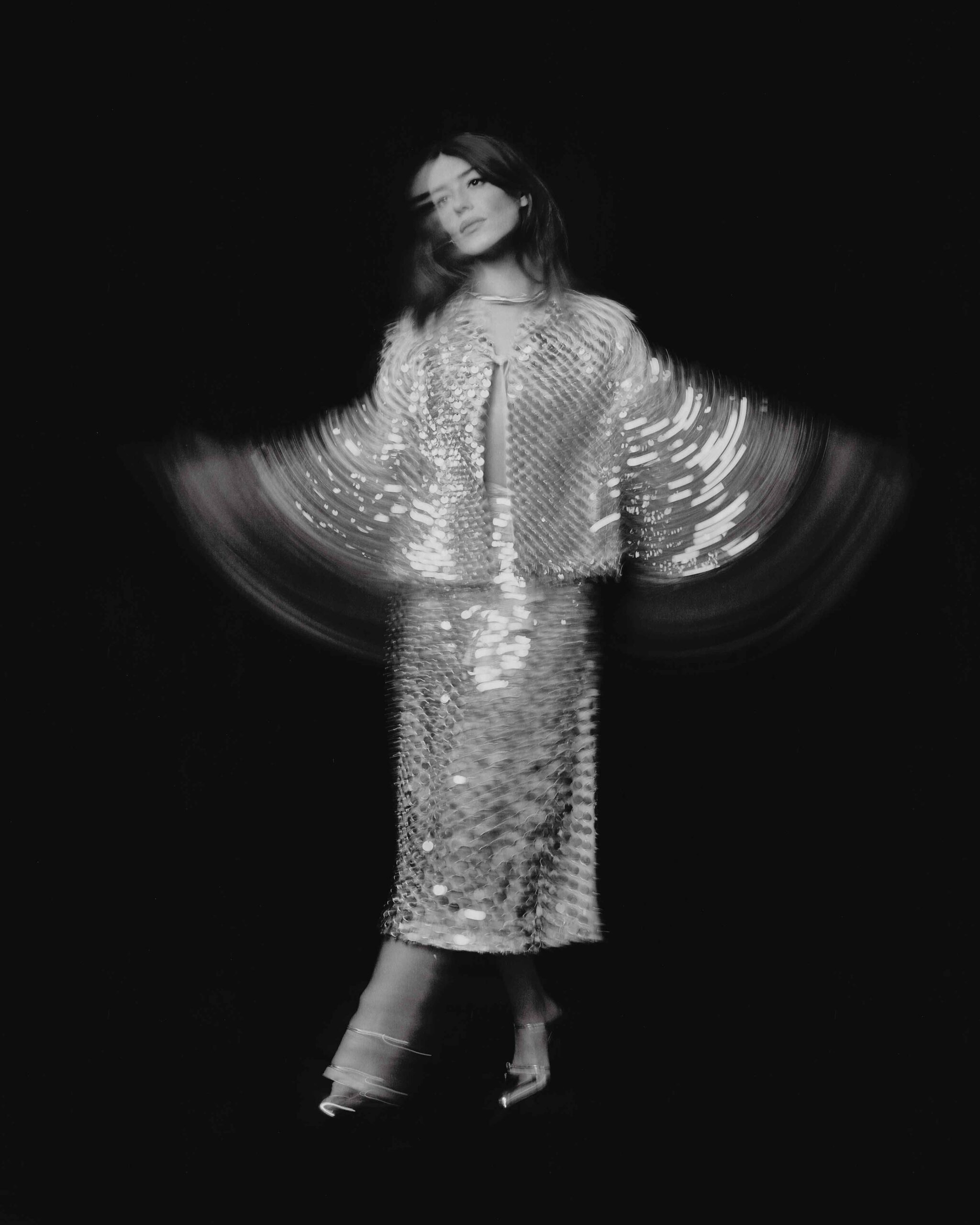 Daisy Edgar-Jones twirling in a shimmering sequin outfit with motion blur against a black background for Flaunt April 2025.