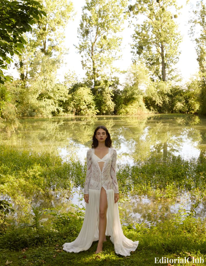 Deva Cassel stands by a tranquil pond in a long, sheer white lace dress with a high slit.