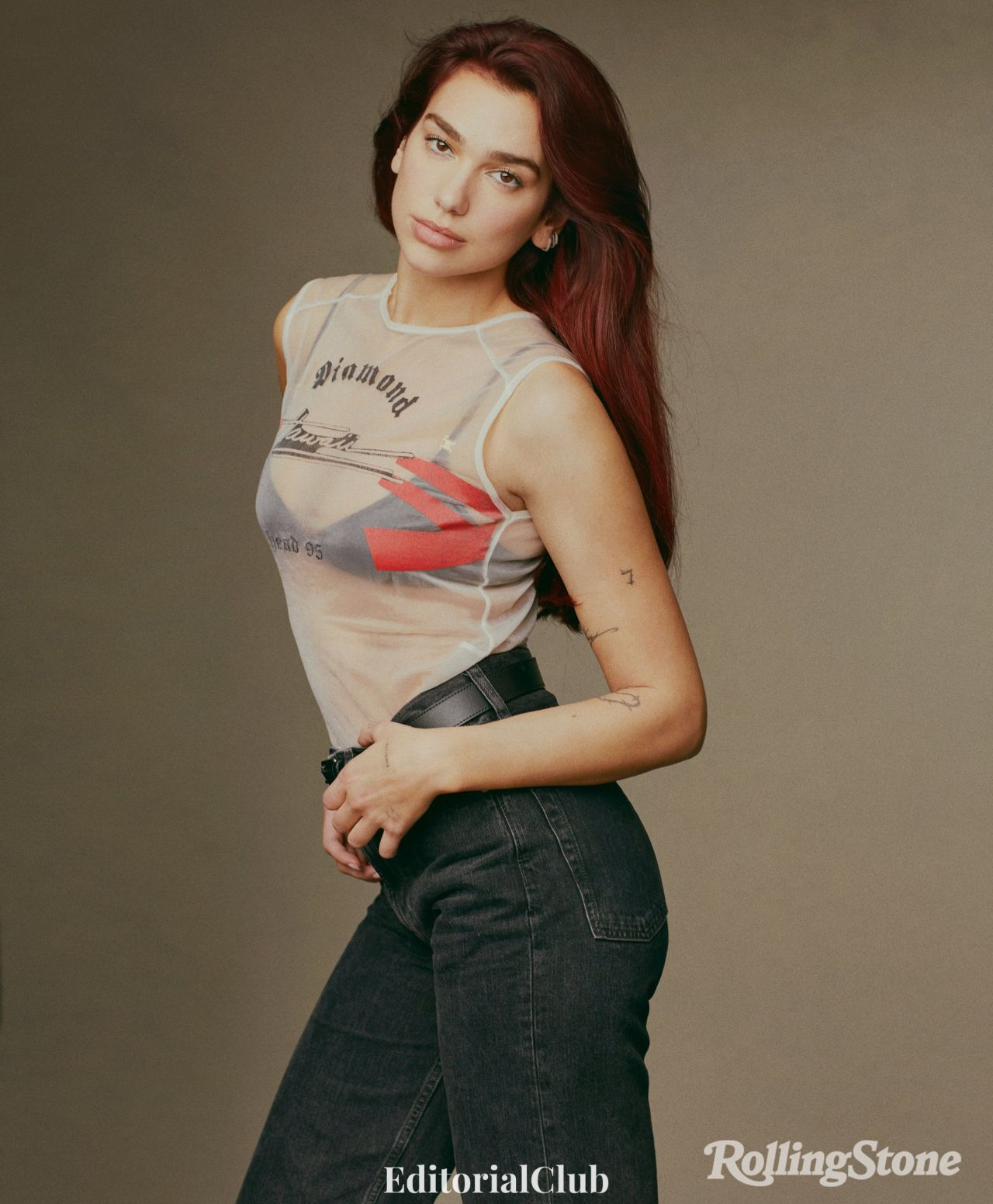 Dua Lipa posing in mesh graphic tank top and high-waisted jeans, styled for Rolling Stone 2024 cover story.