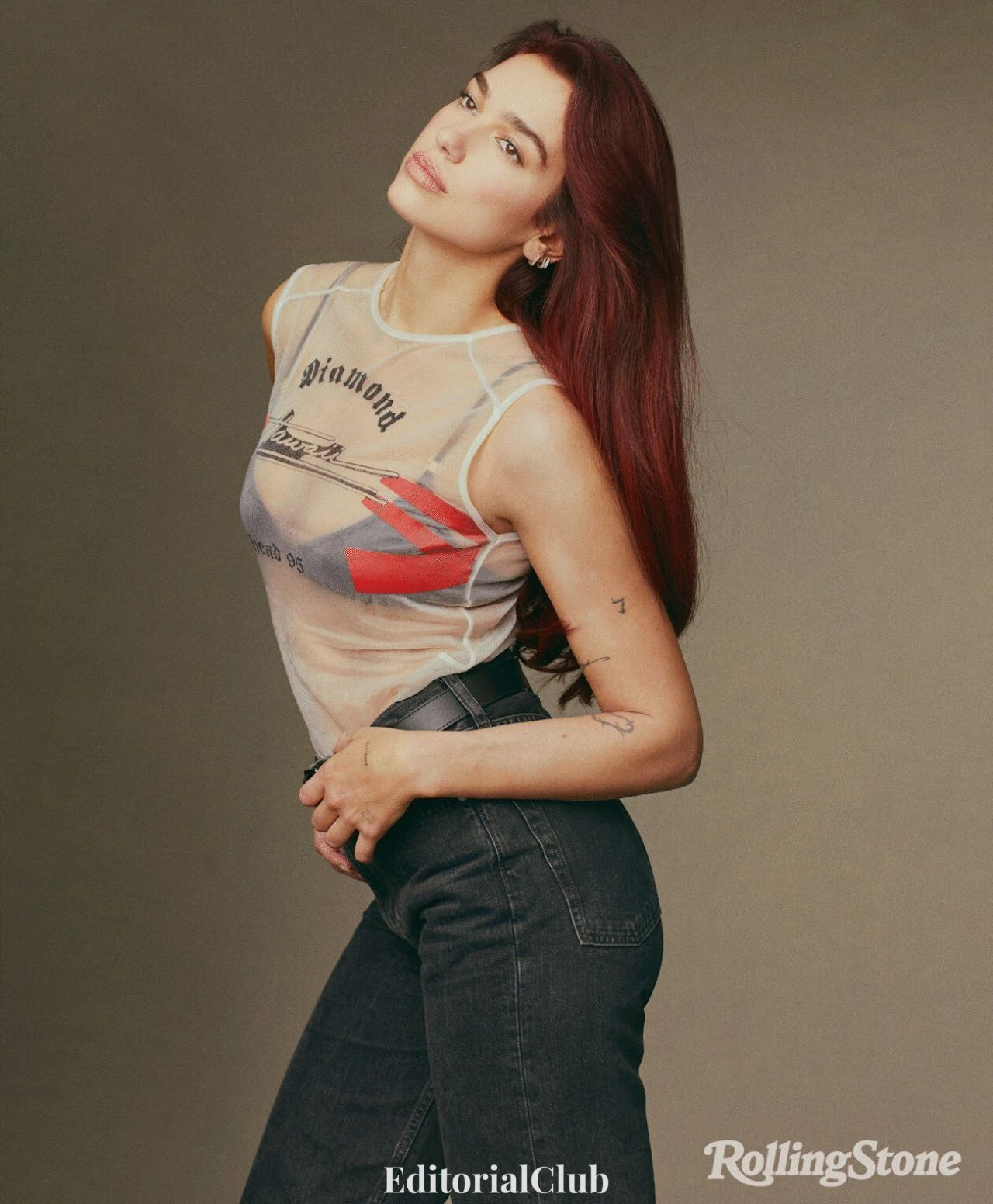 Dua Lipa wearing a sheer tank top and high-waisted jeans with red hair in a casual Rolling Stone look