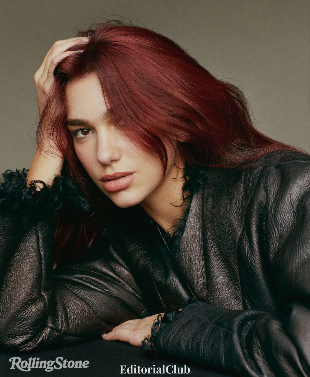 Dua Lipa resting her head on her hand in a textured leather jacket for her Rolling Stone editorial