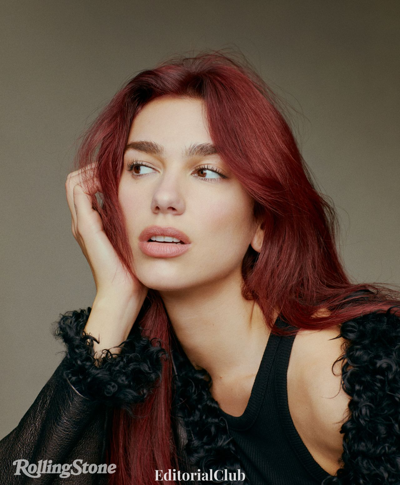 Dua Lipa gazing thoughtfully in a black tank and curly-trimmed jacket from Rolling Stone January 2024