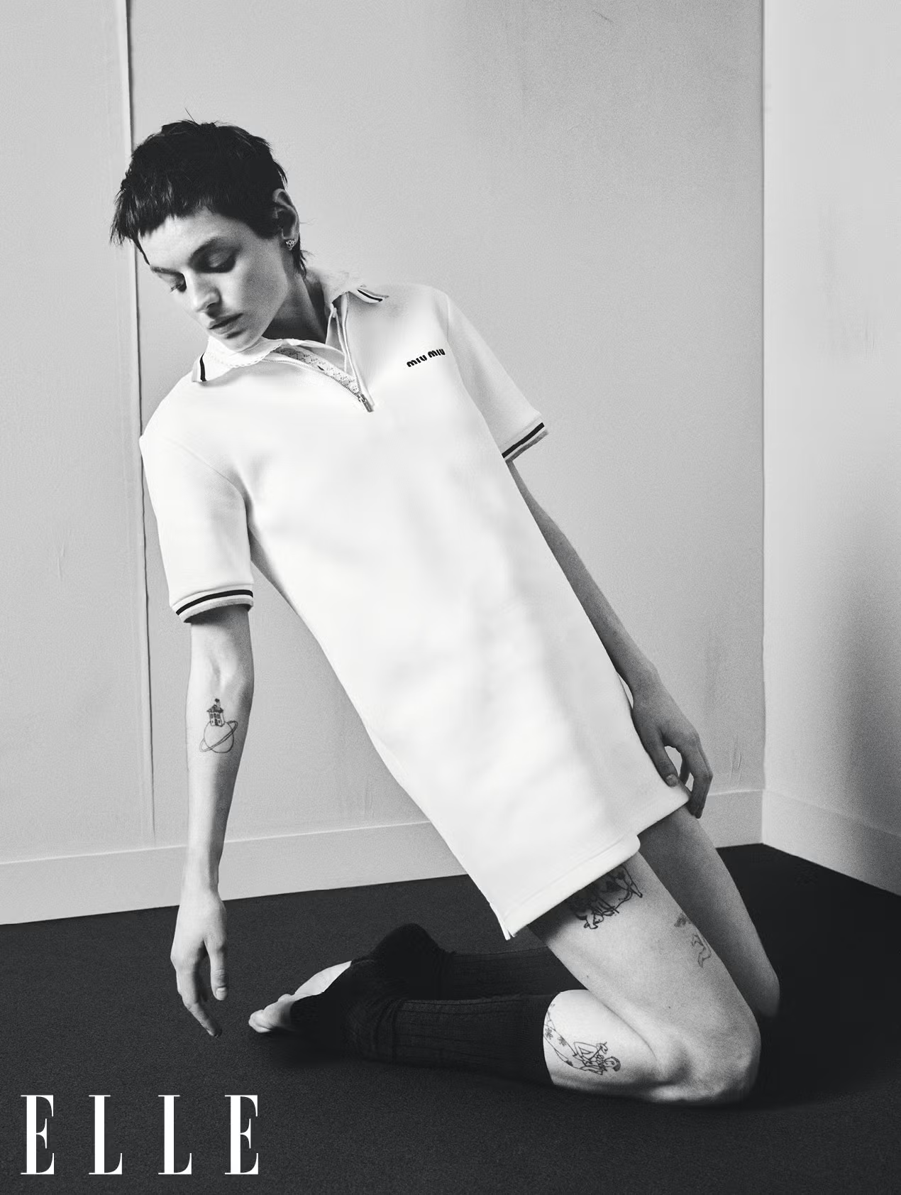 Emma Corrin kneels in a minimalist black-and-white shot wearing Miu Miu polo dress and mid-calf socks for ELLE UK April 2025