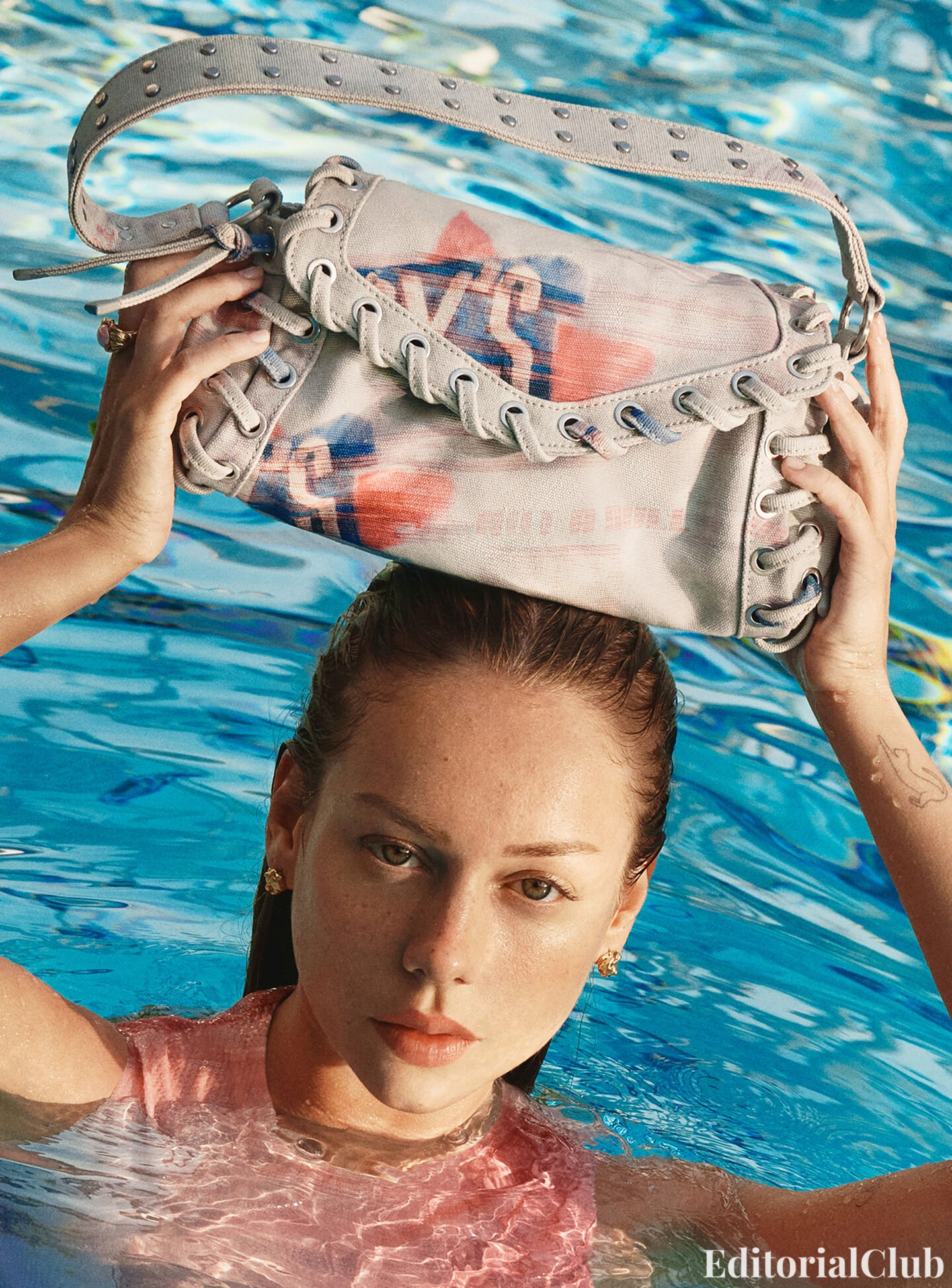 Close-up of Ester Expósito in a pool holding a denim Desigual bag on her head with bold grommet details