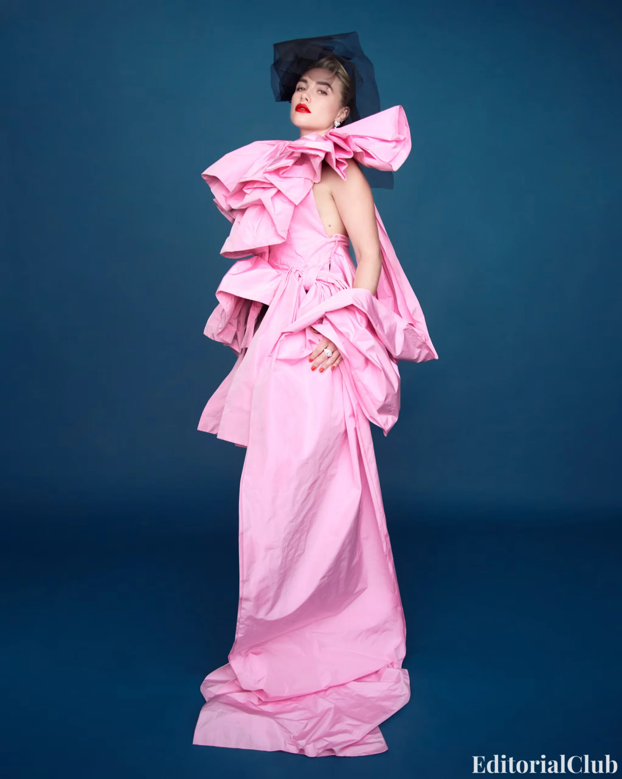 Florence Pugh in a voluminous pink gown with oversized ruffles and black headpiece, posing confidently.