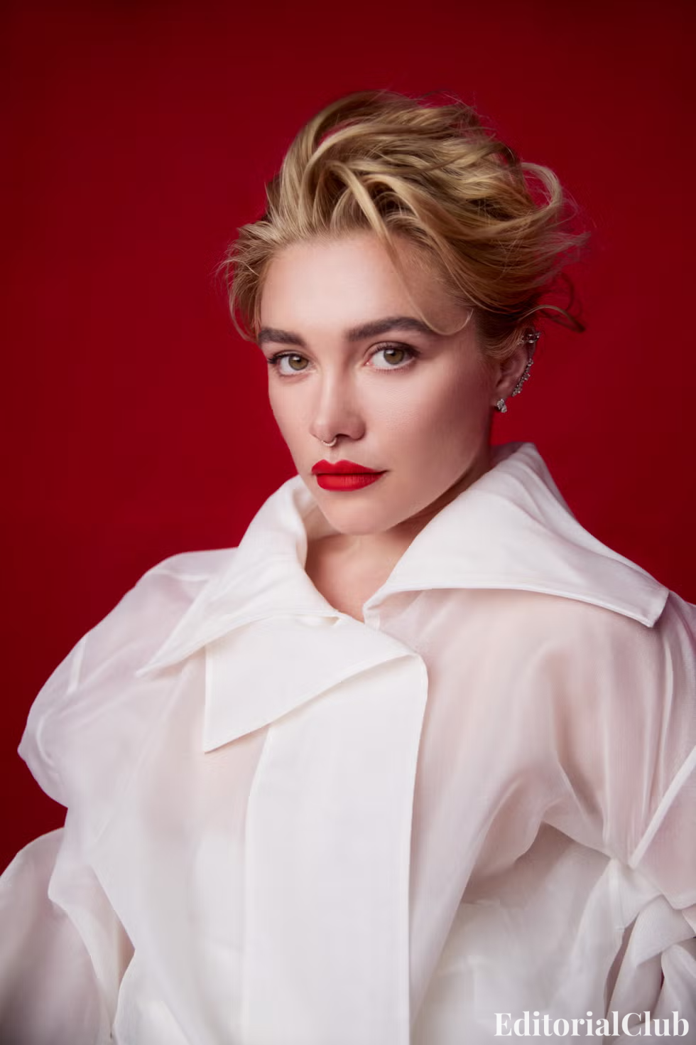 Florence Pugh in a sheer white blouse with oversized collar, against a striking red background.