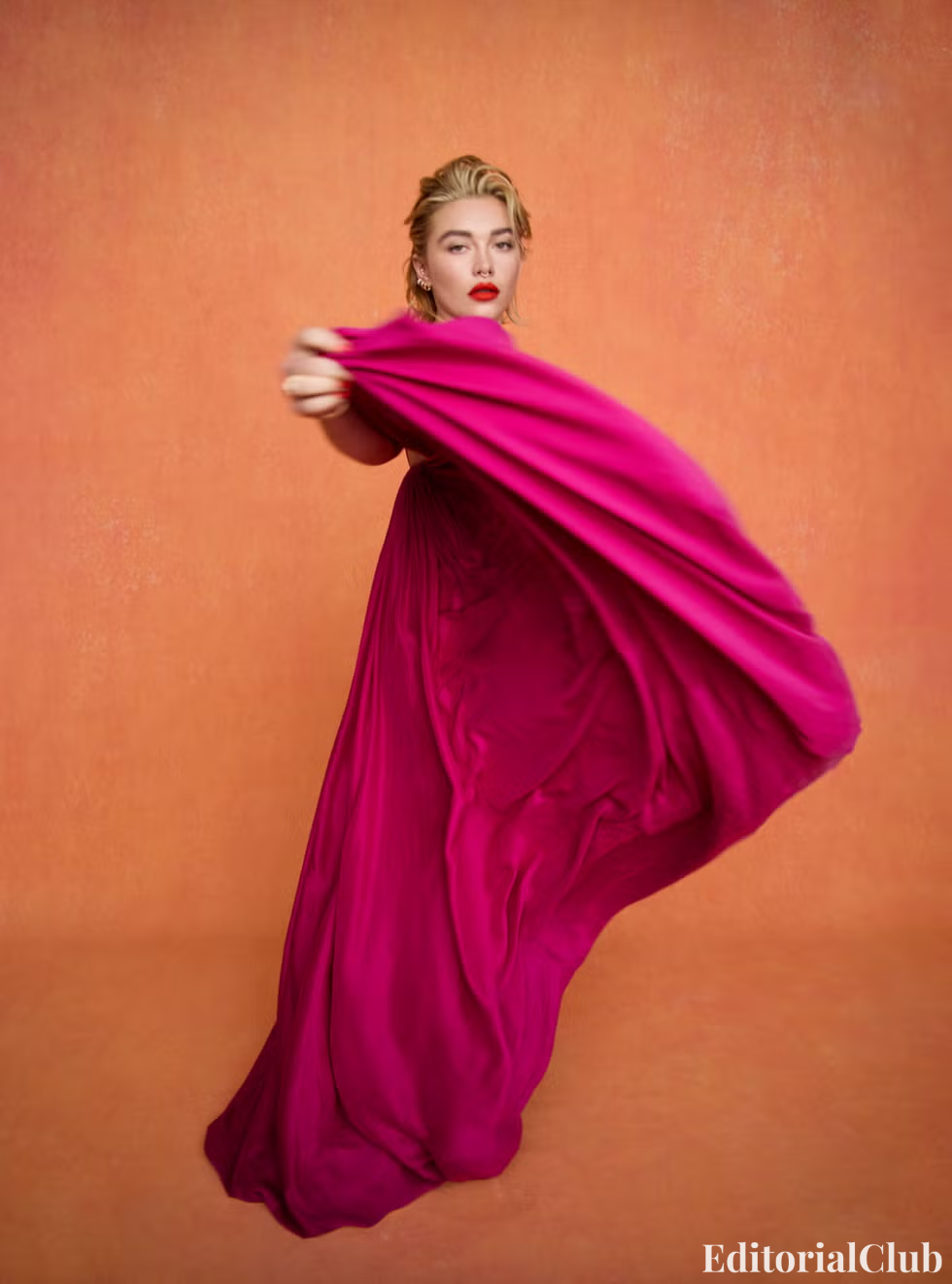 Florence Pugh in a flowing magenta gown mid-motion, posed against a burnt orange wall.