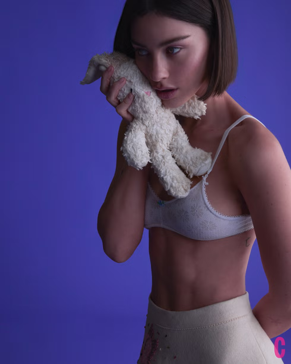 Gracie Abrams holds a plush toy close to her face while wearing a white bralette and high-waisted skirt for Cosmopolitan February 2025.