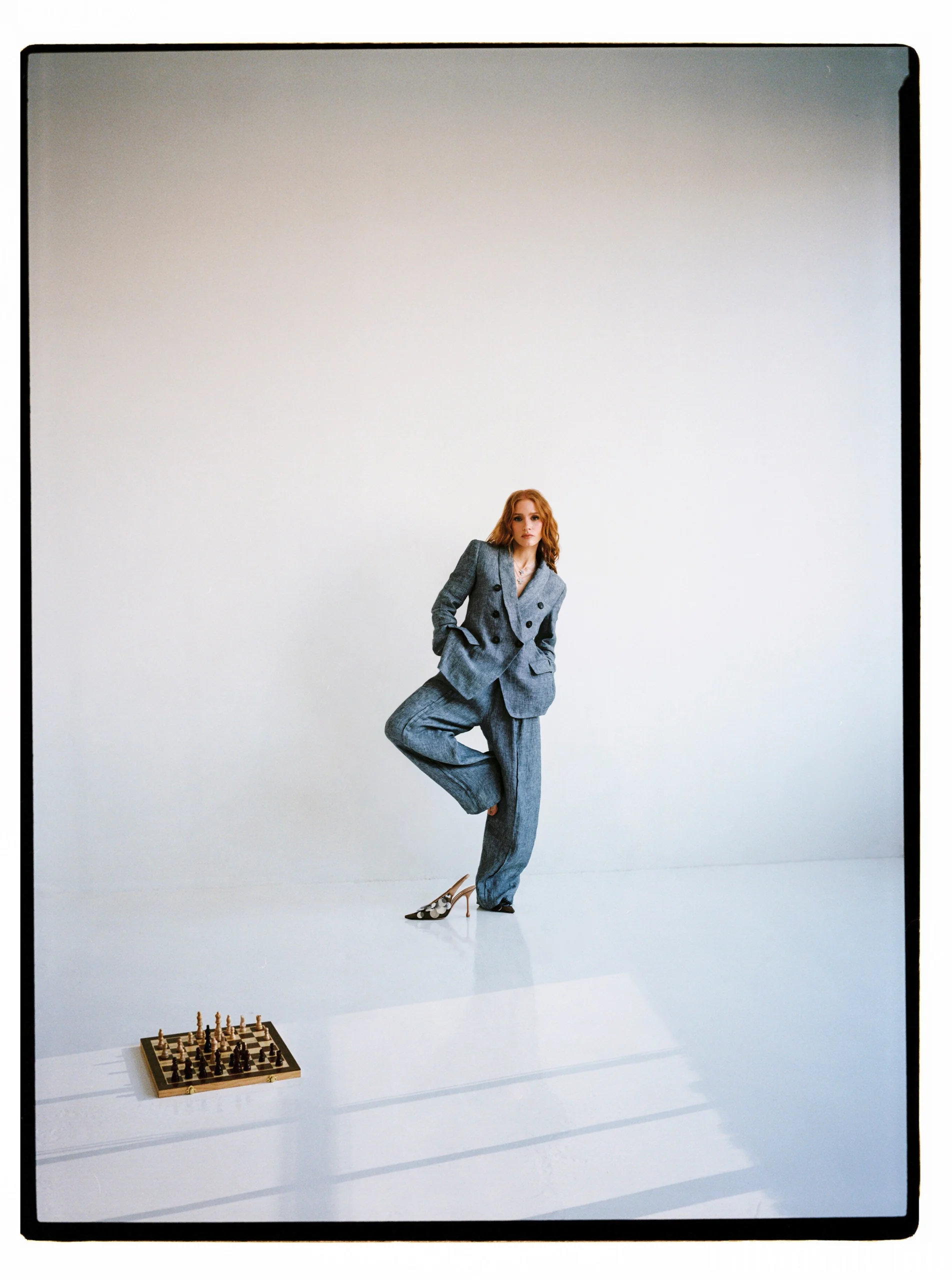 Jessica Chastain standing in a grey pantsuit next to a chessboard for ELLE Spain April 2025 minimalist studio photo