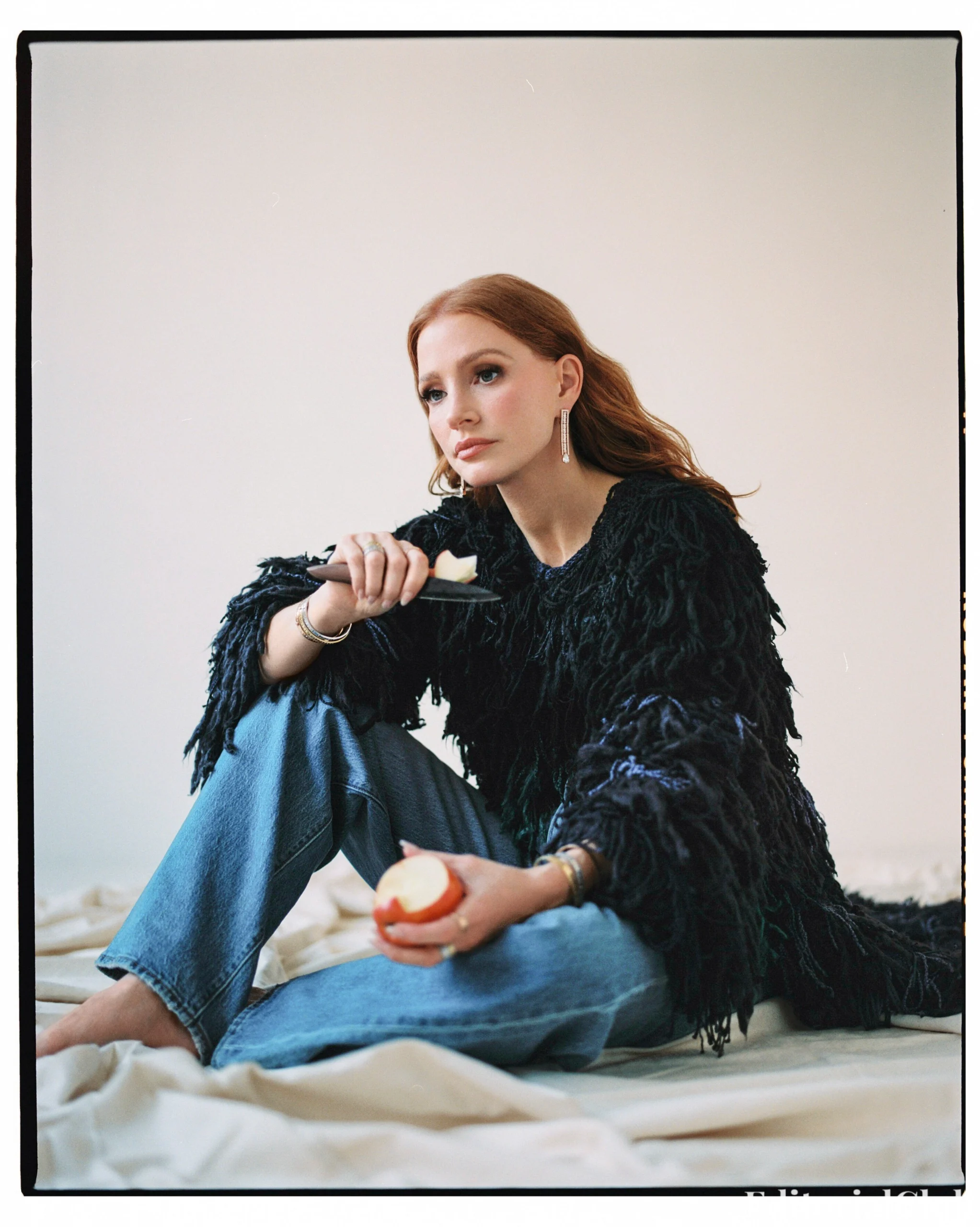 Jessica Chastain eating an apple in a textured black sweater and jeans for ELLE Spain April 2025 casual editorial