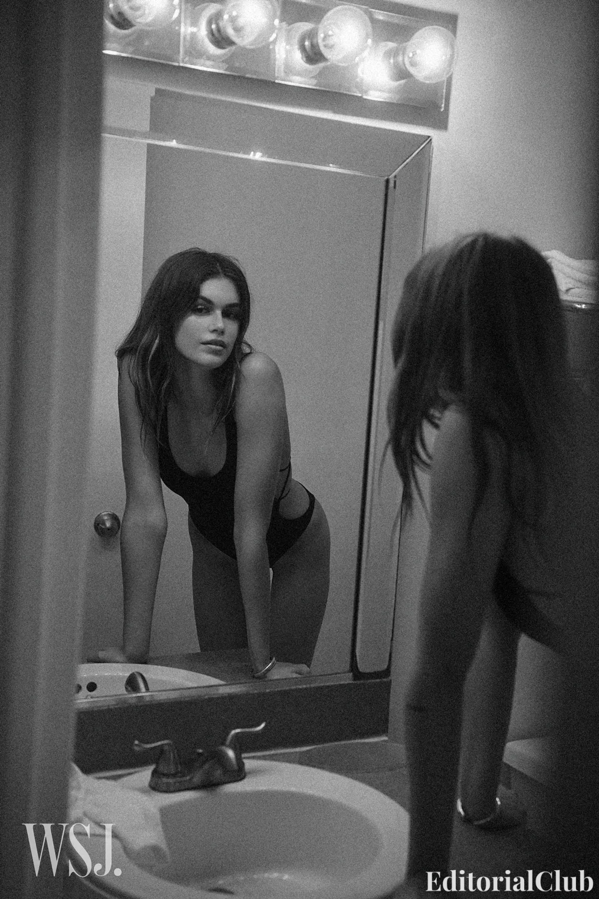 Kaia Gerber posing in front of a bathroom mirror wearing a black swimsuit, captured in cinematic black and white for WSJ Magazine Spring 2024.
