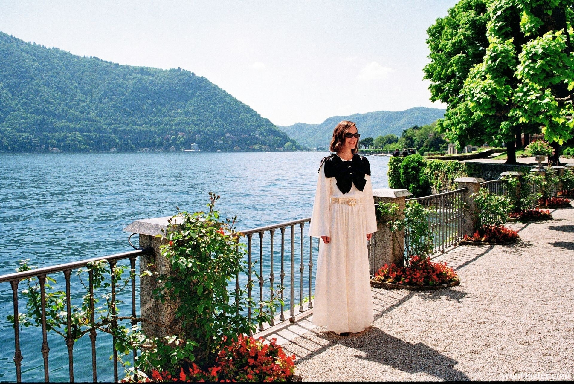 Keira Knightley poses in a long white Chanel dress with oversized black bow details by Lake Como during the Chanel Cruise 2025 show, photographed for British Vogue.