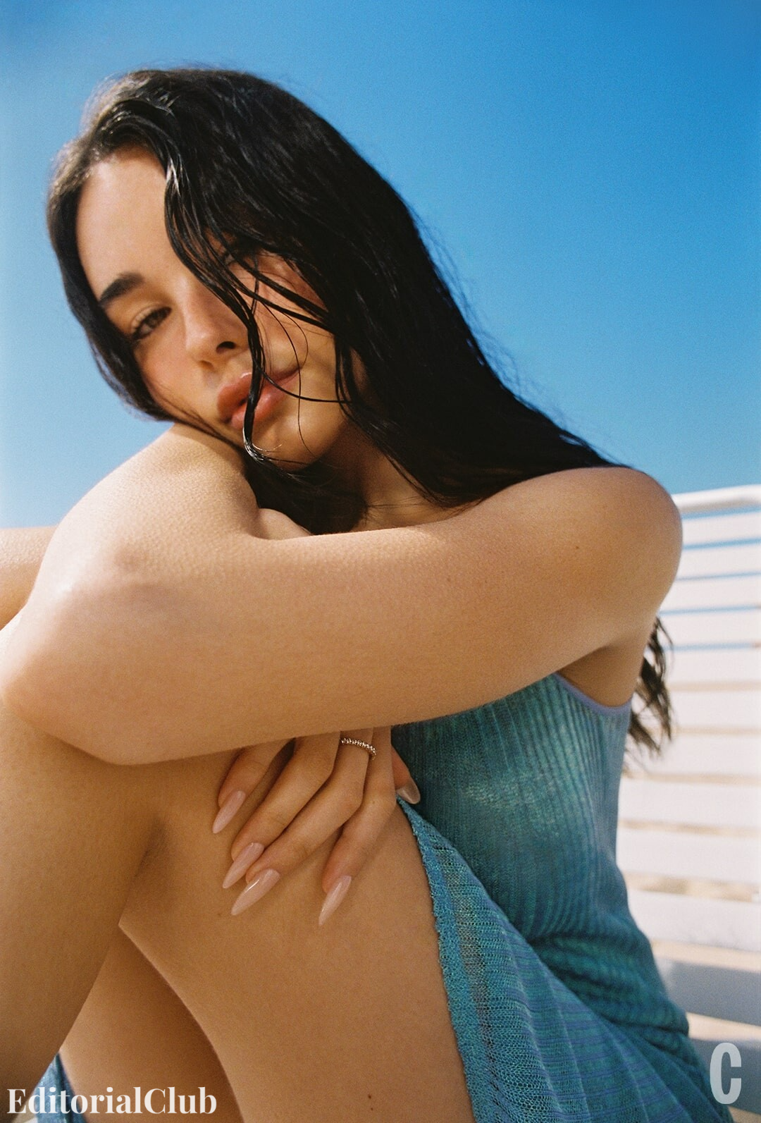 Madison Beer posing under the sun in a blue textured dress, with wet hair and a close-up view of her face and hands.
