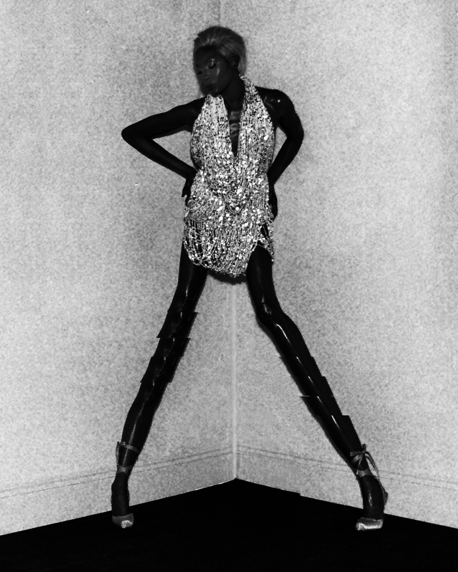 Naomi Campbell strikes a bold pose in a corner wearing a crystal-embellished mini dress and extreme platform heels in a dramatic black-and-white shot for i-D Magazine March 2025.
