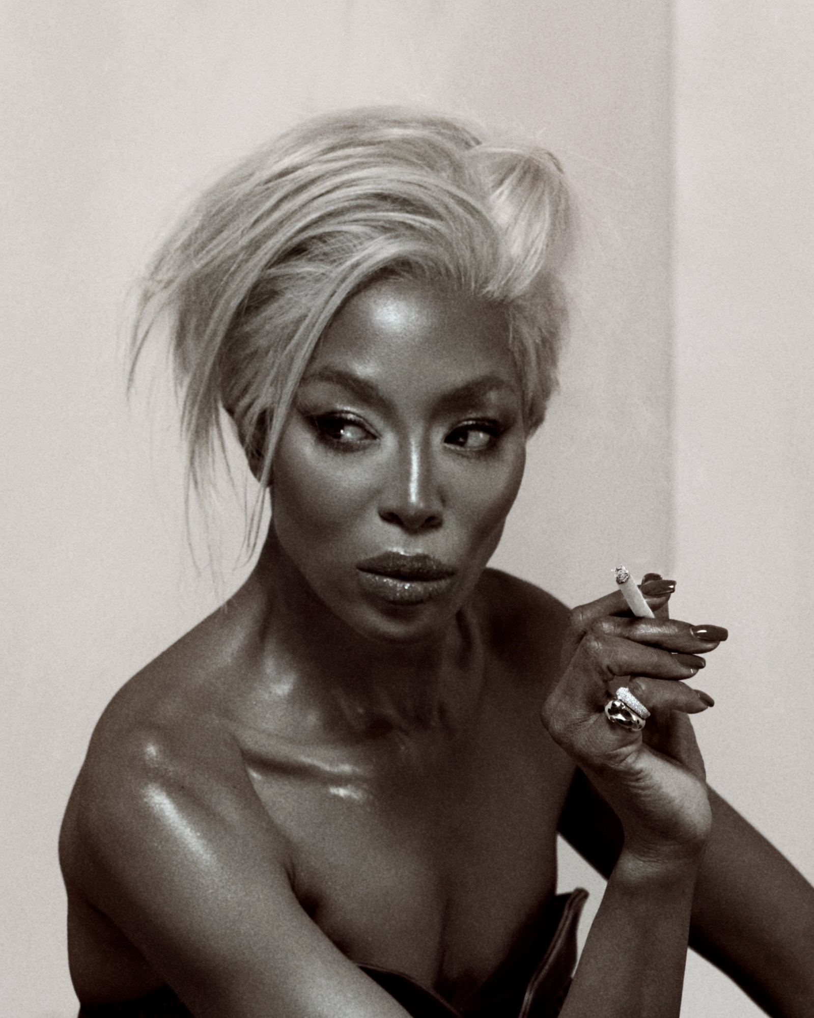 Naomi Campbell with platinum blonde hair styled voluminously, holding a cigarette in a vintage-toned editorial shot for i-D Magazine.