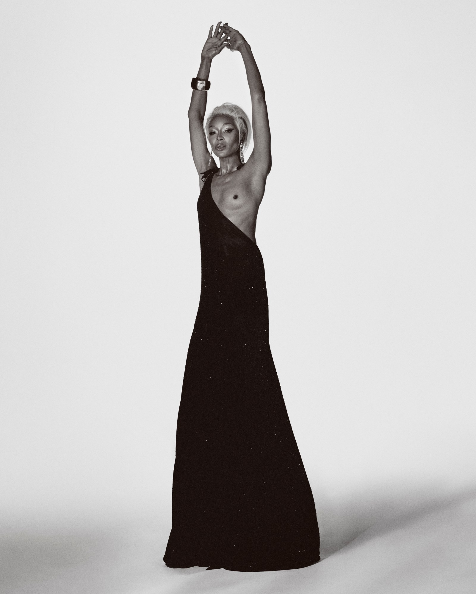 Naomi Campbell raises her arms while wearing a sheer black gown in a powerful studio shot for i-D Magazine March 2025.