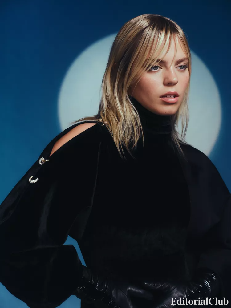 Renee Rapp in a black velvet top with cut-out shoulders, photographed against a soft moonlit blue background